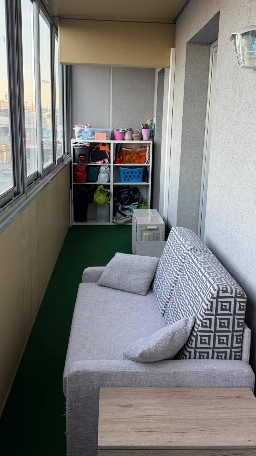 Gemütlicher, verglaster Balkon mit Sitzgelegenheiten und praktischen Regalen für zusätzlichen Stauraum.