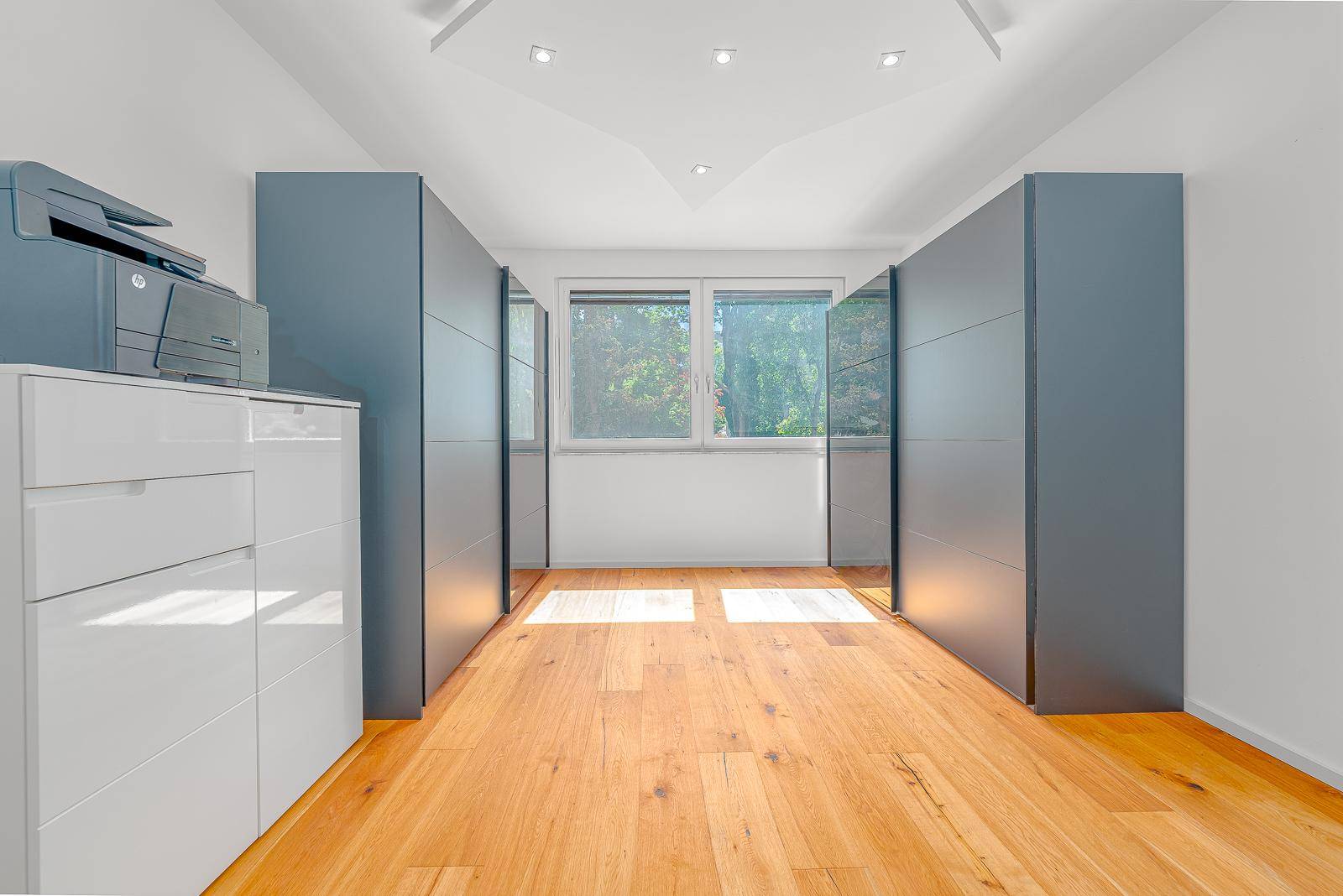 Helles Zimmer mit Holzboden und modernen, blaugrauen Einbauschränken.