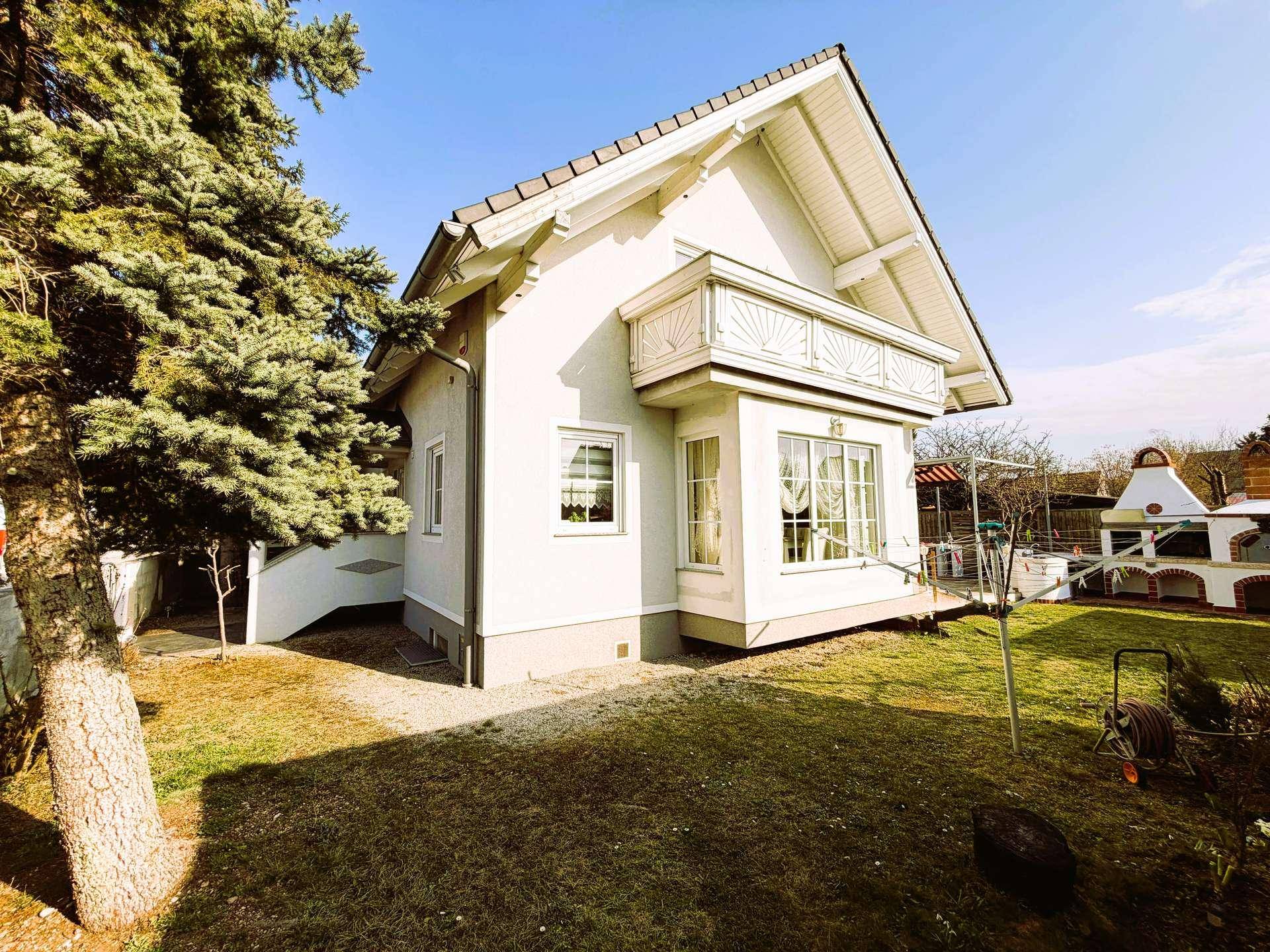 Seitenansicht des Hauses mit Erker und Garten, inklusive eines gemauerten Grills im Hintergrund.