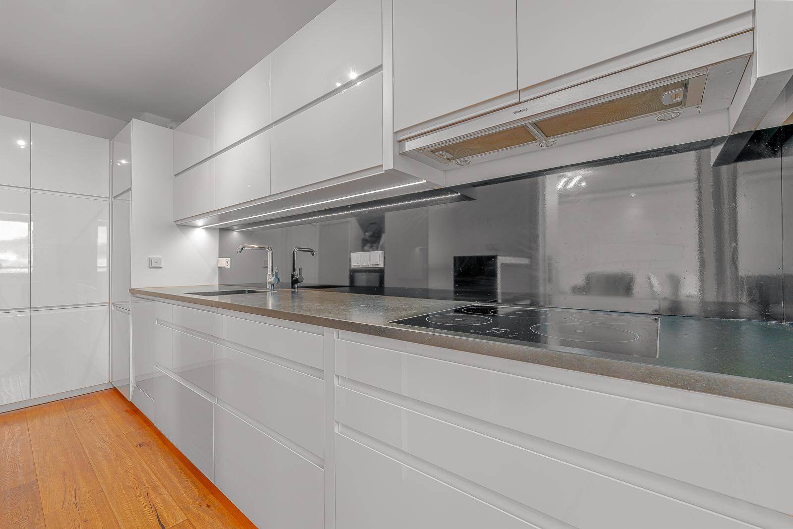Moderne Küche mit weißen Hochglanzfronten, dunkler Arbeitsplatte und Induktionskochfeld.