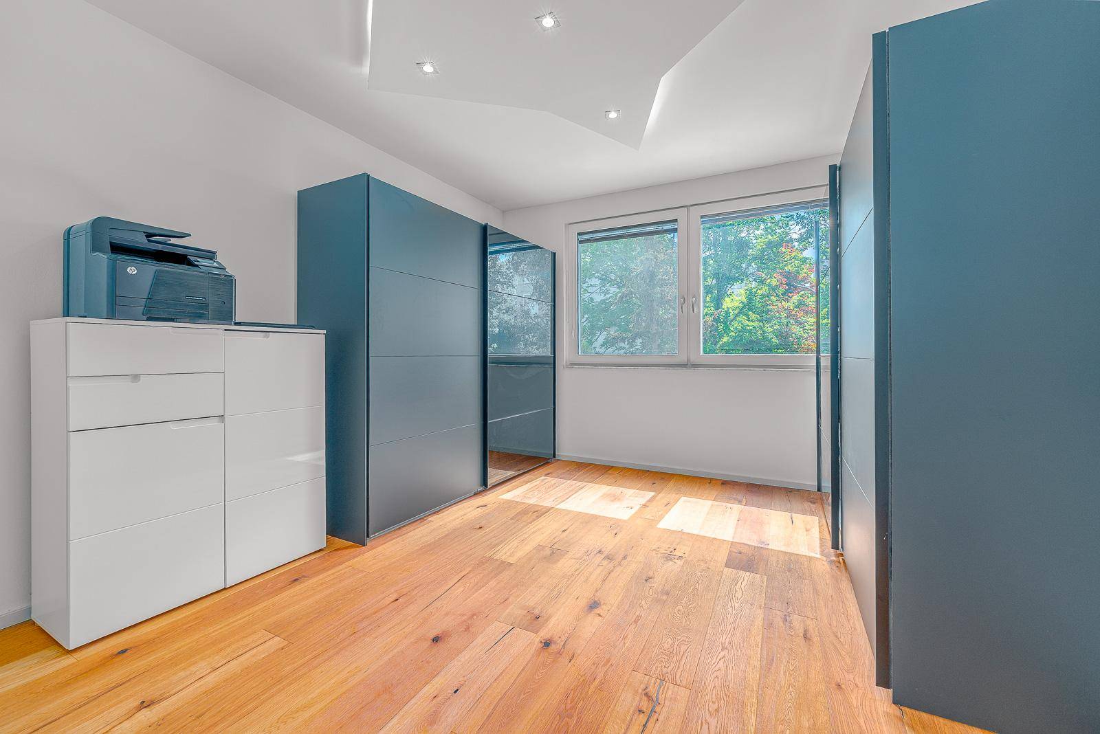 Helles Zimmer mit Holzboden und modernen, blaugrauen Einbauschränken.