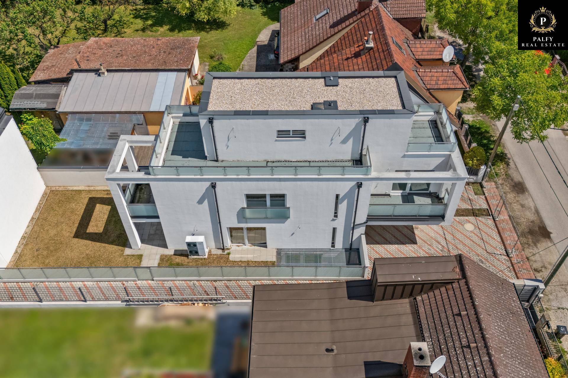 Draufsicht auf das moderne Gebäude mit Flachdach und angrenzendem Gartenbereich, umgeben von Nachbarhäusern.