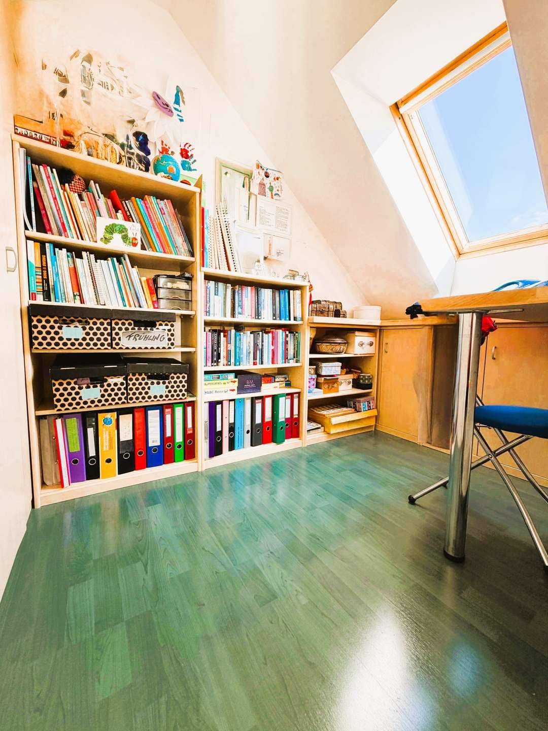 Helles Arbeitszimmer im Dachgeschoss mit Bücherregalen, Schreibtisch und einem Dachfenster für viel Tageslicht.