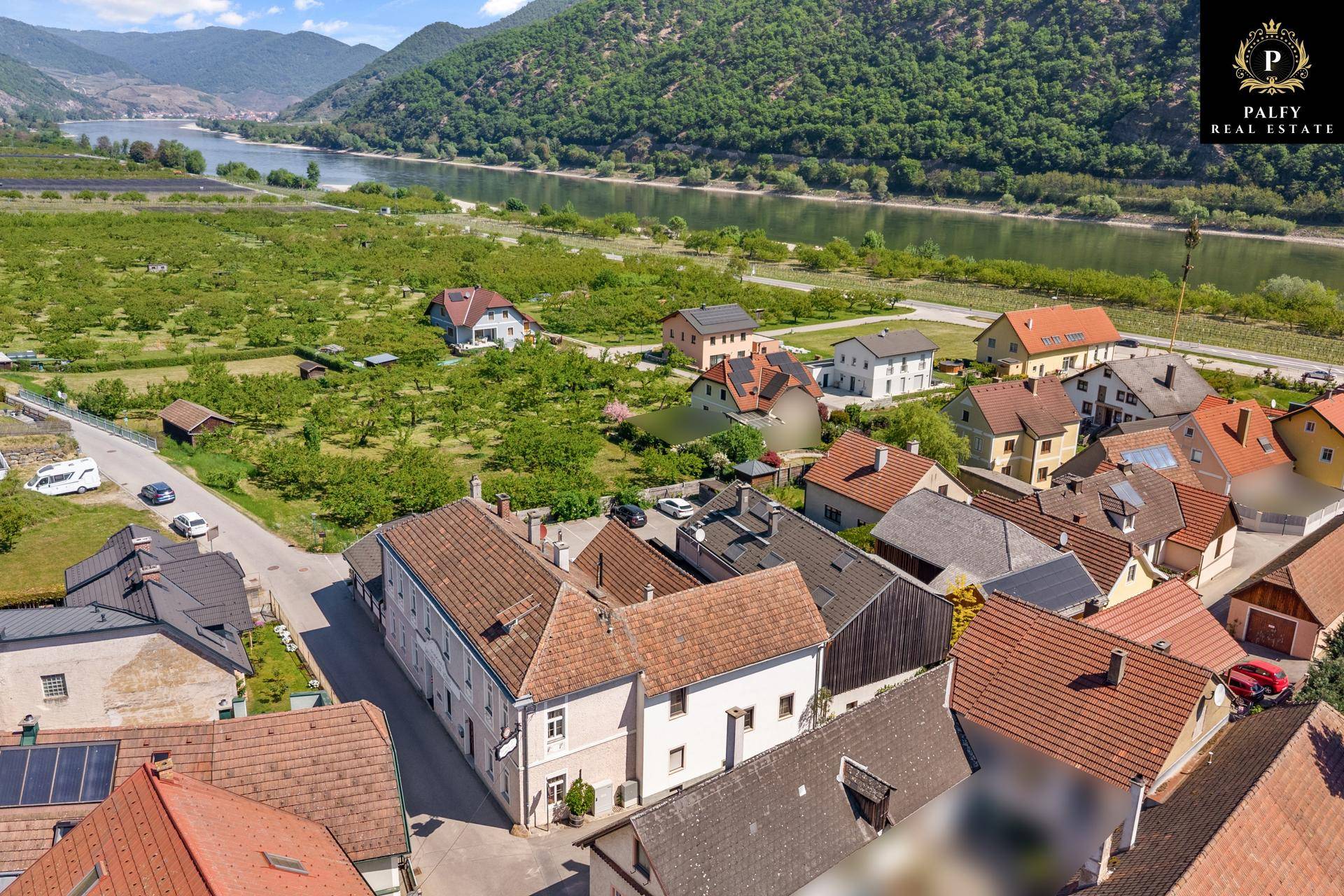 Vogelperspektive eines Dorfes mit vielen Dächern, umgeben von Weinbergen und einem Fluss.