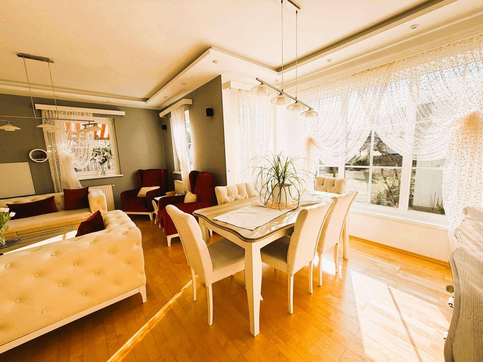 Eleganter Essbereich mit großem Tisch, hellen Stühlen und viel Tageslicht durch große Fenster.