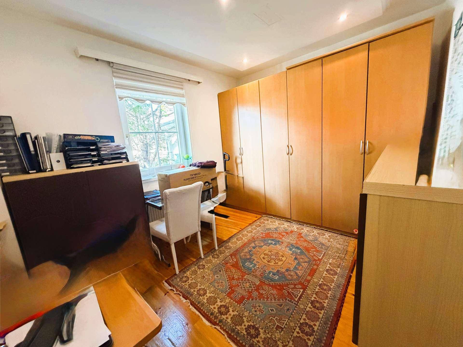 Helles Zimmer mit Holzschrank, Schreibtisch und einem farbenfrohen Teppich, ideal als Schlaf- oder Arbeitszimmer.