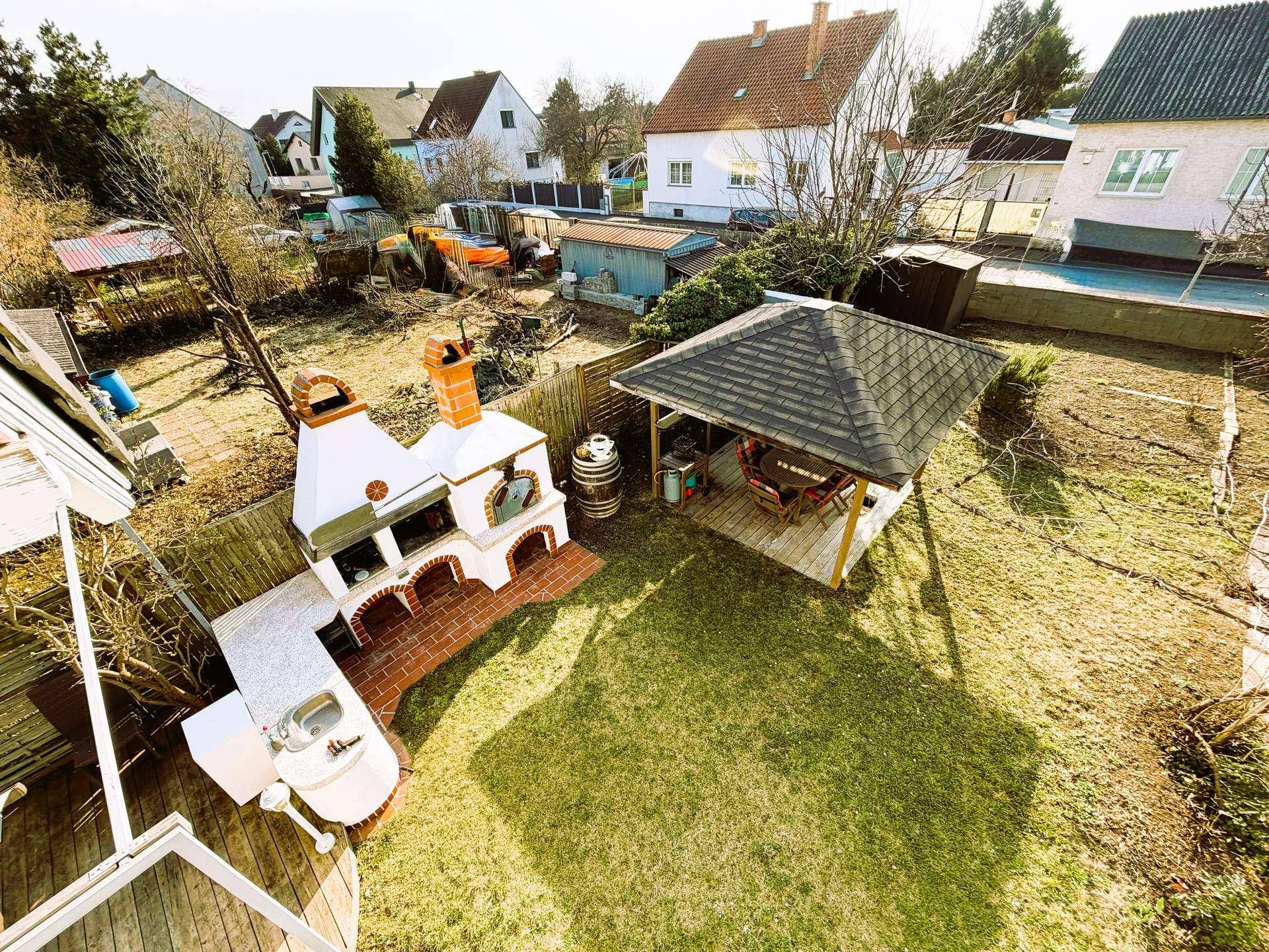Luftaufnahme des Gartens mit großer Außenküche, Grill und Pavillon, umgeben von Grünflächen.