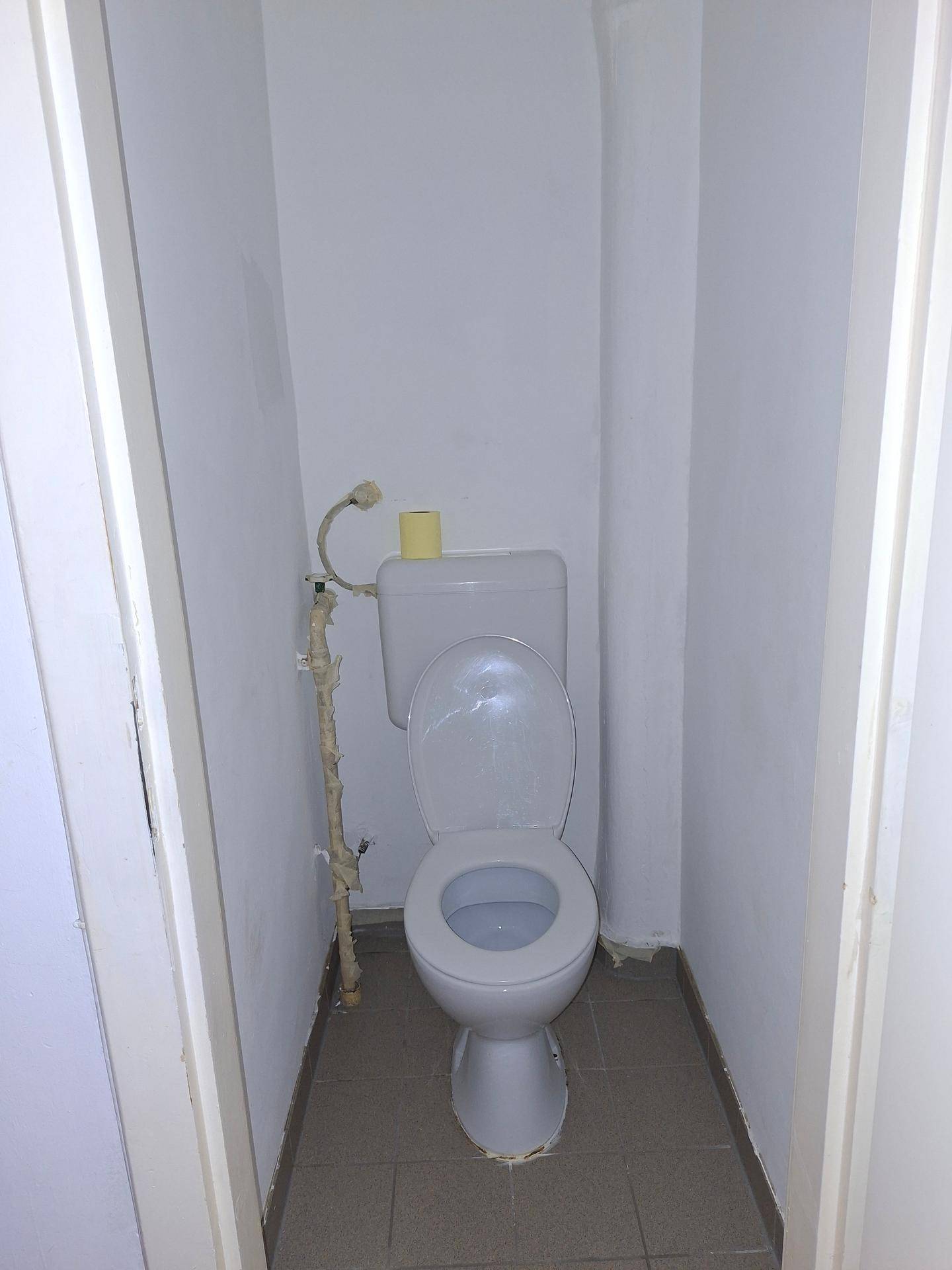 Kleines WC mit Toilette und Fliesenboden in einem schmalen Raum.