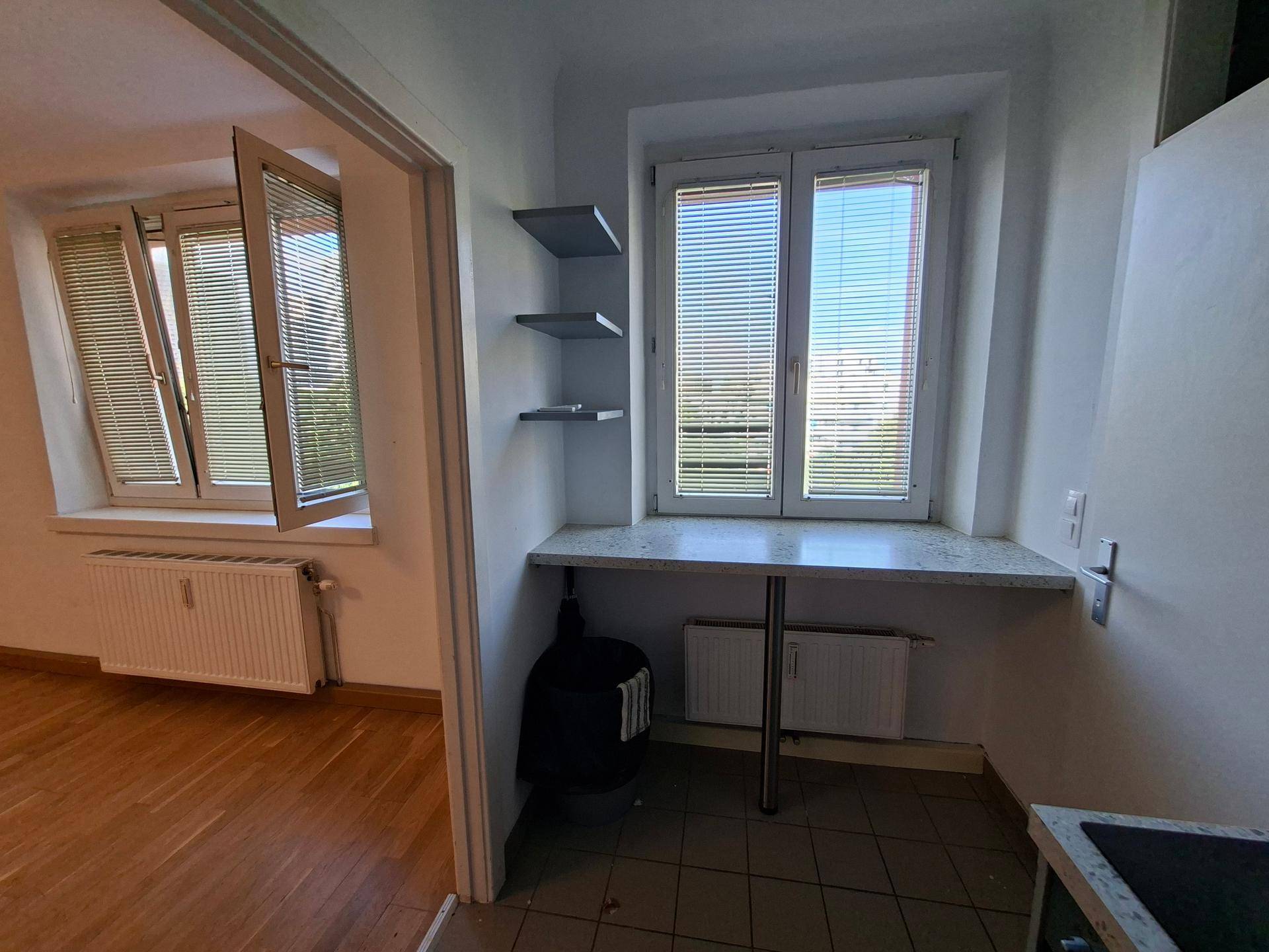 Kleiner Bereich mit Arbeitsplatte unter einem Fenster, angrenzend an einen Raum mit Holzboden.