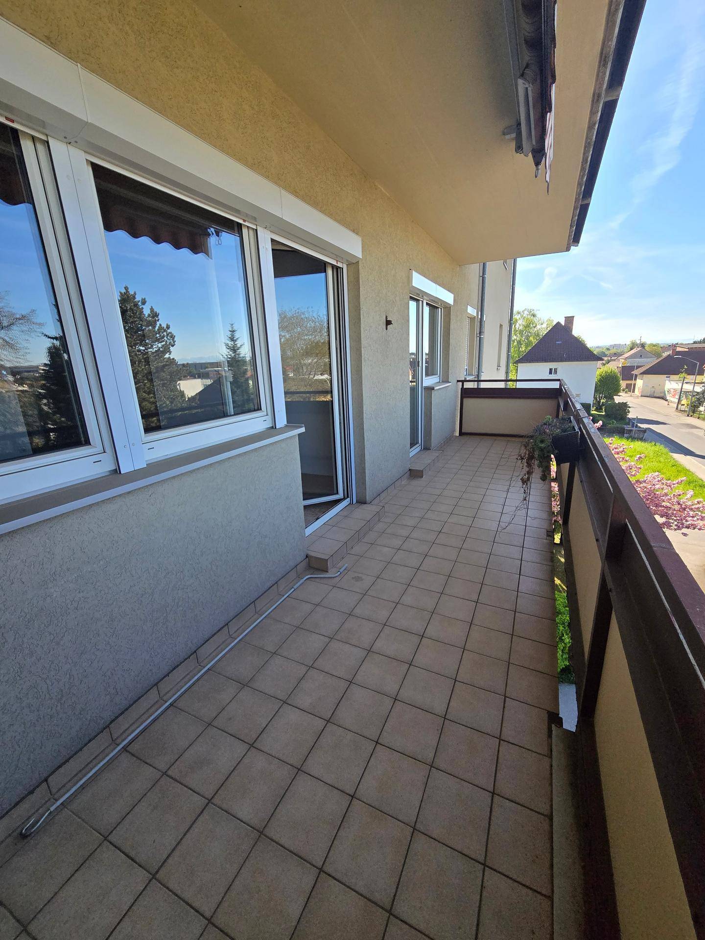 Langer Balkon mit Fliesenboden und einem Ausblick ins Grüne.