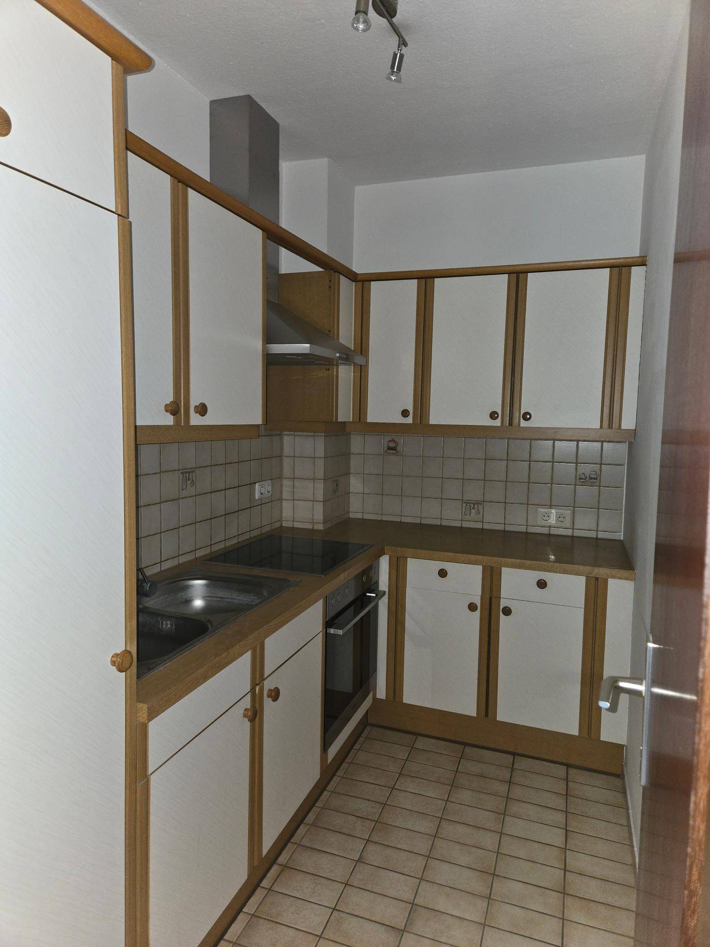 Funktionale Einbauküche mit weißen Schränken, Holzrahmen und Fliesenboden.