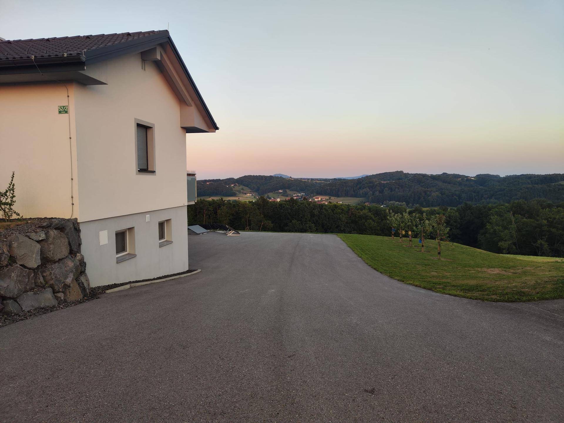 Seitenansicht des Hauses mit weitläufiger Auffahrt und Panoramablick in die hügelige Landschaft.