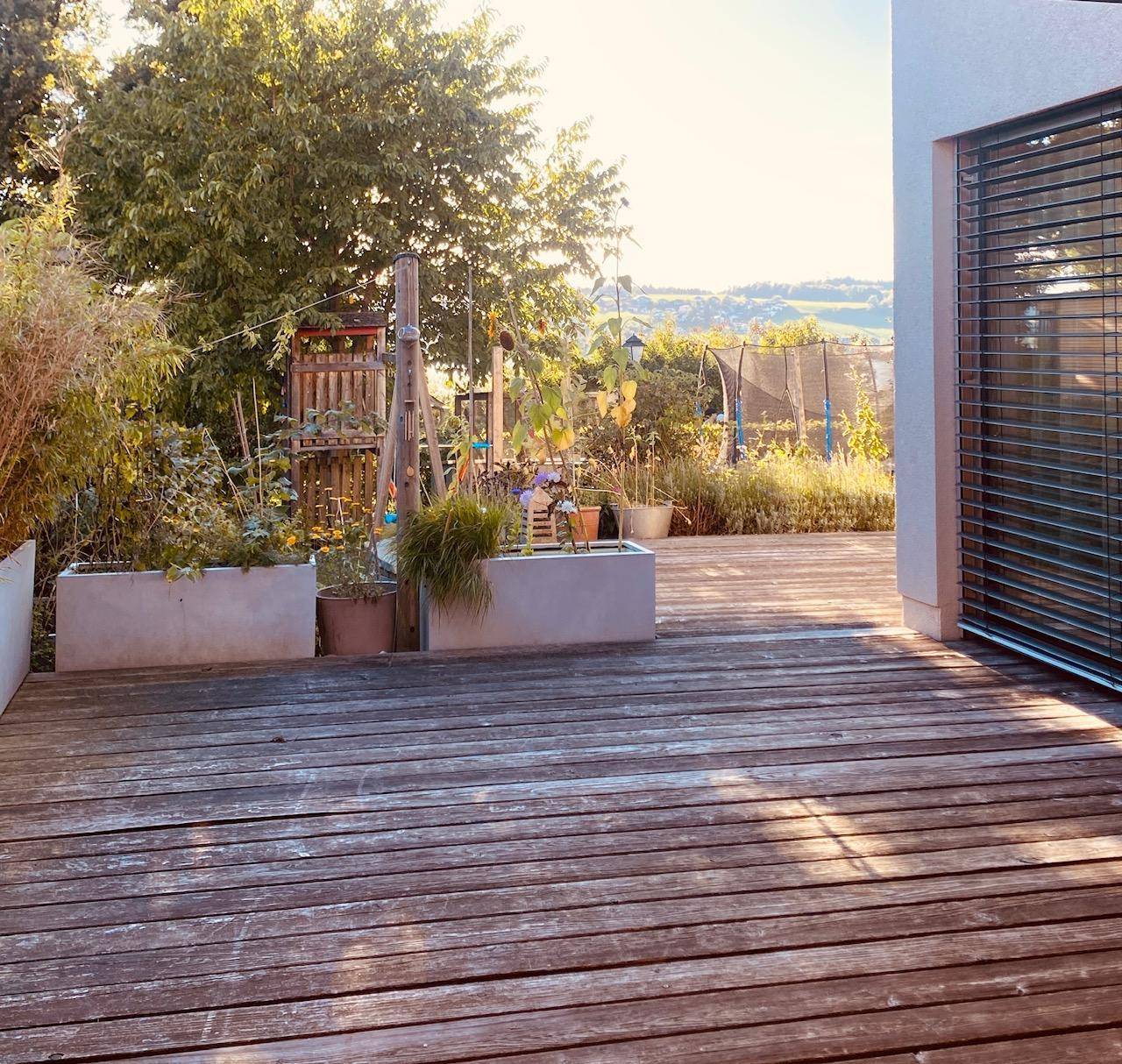 Geräumige Holzterrasse mit Pflanzenkübeln und weitem Blick über die Landschaft.