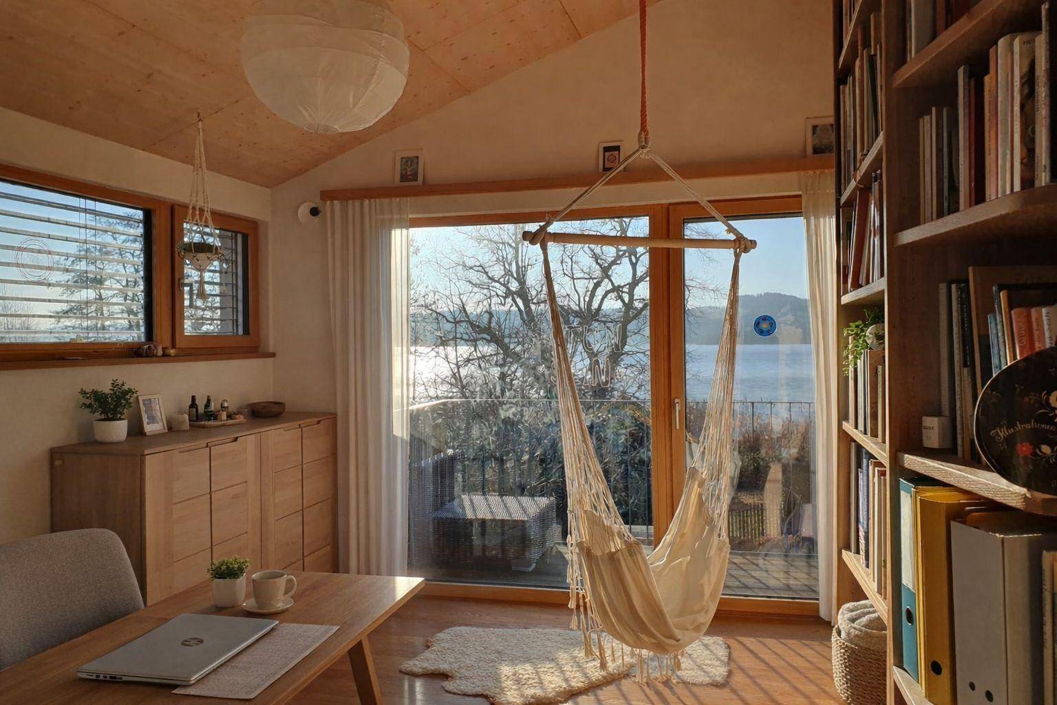 Helles Arbeitszimmer mit Seeblick, Bücherregalen und einem gemütlichen Hängesessel am Fenster.