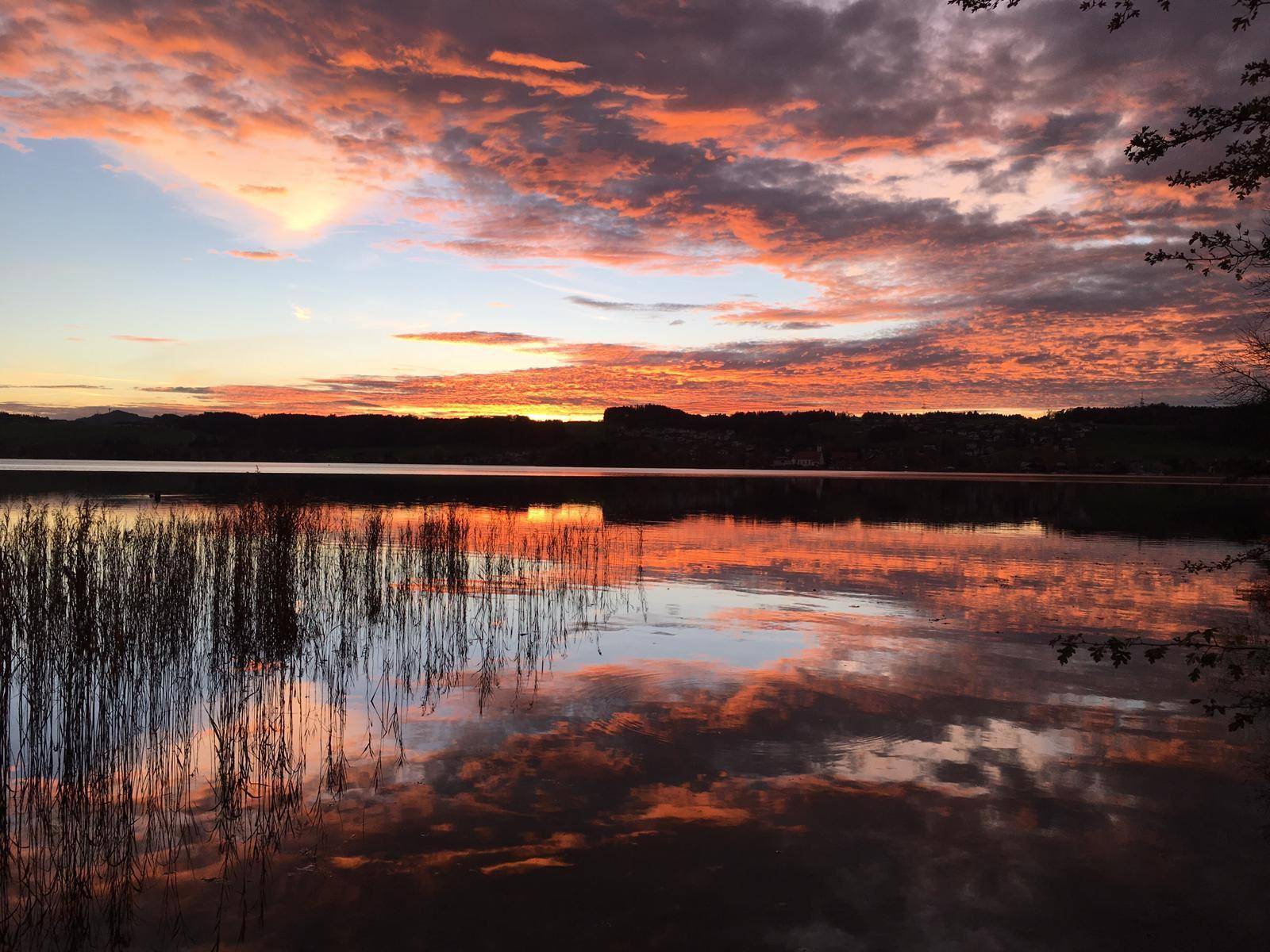 Farbenprächtiger Sonnenuntergang über dem See mit dramatischen Wolken und Spiegelungen im Wasser.