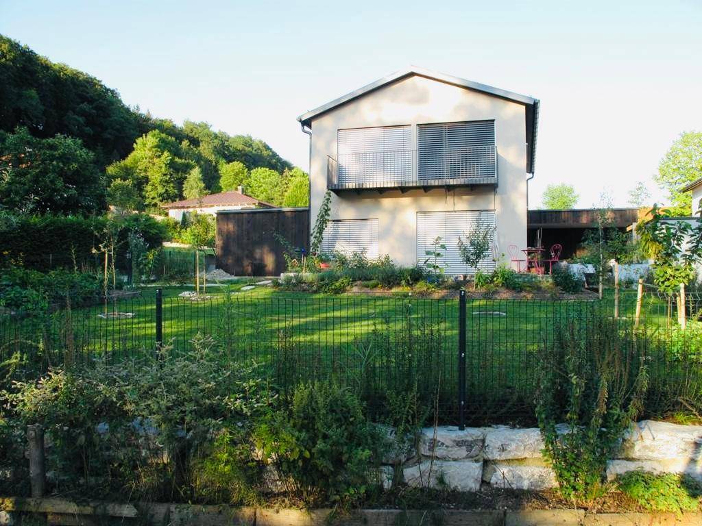 Einfamilienhaus mit gepflegtem Garten und Balkon, umgeben von viel Grün an einem sonnigen Tag.