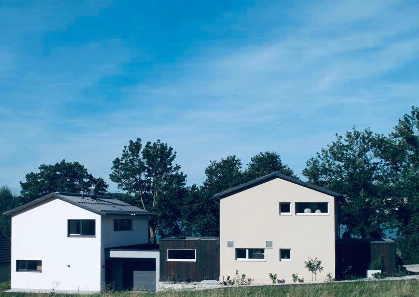 Zwei moderne Einfamilienhäuser mit schlichter Architektur und großen Fenstern in ländlicher Umgebung.
