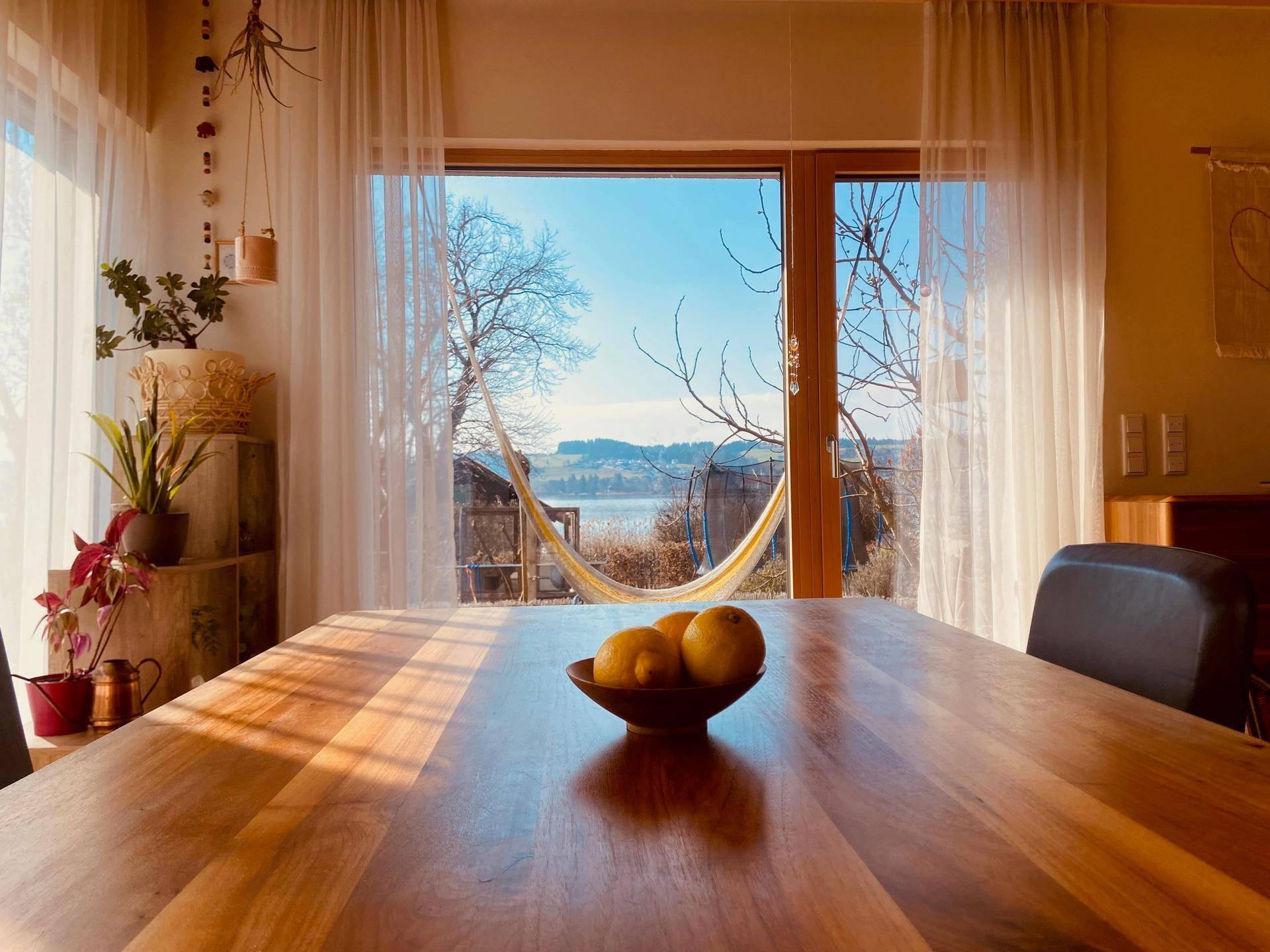Heller Essbereich mit Holztisch und großzügigem Blick auf den See und die umliegende Landschaft.