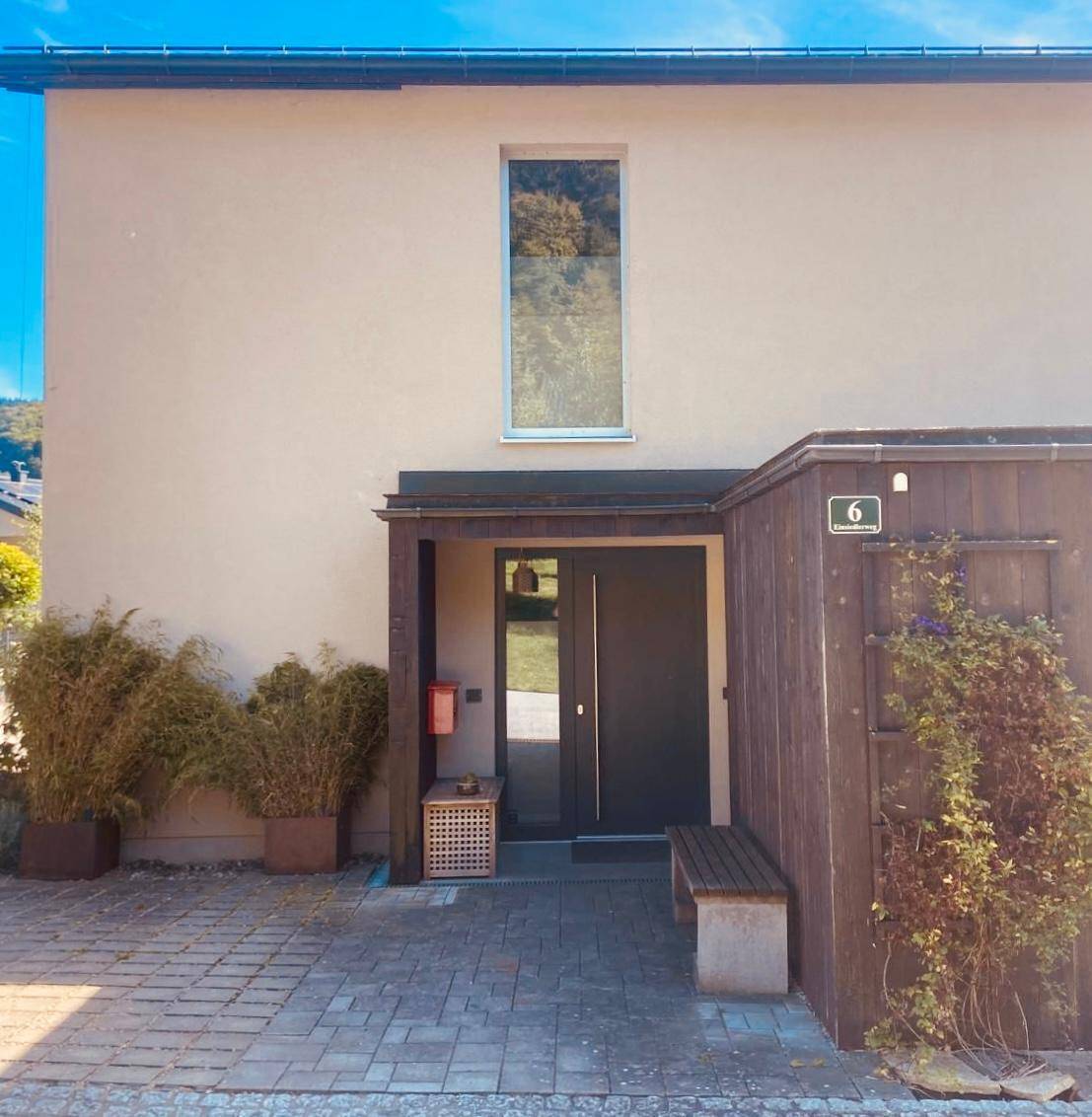 Moderner Hauseingang mit Holzelementen, einer Sitzbank und einer hohen Fensternische.
