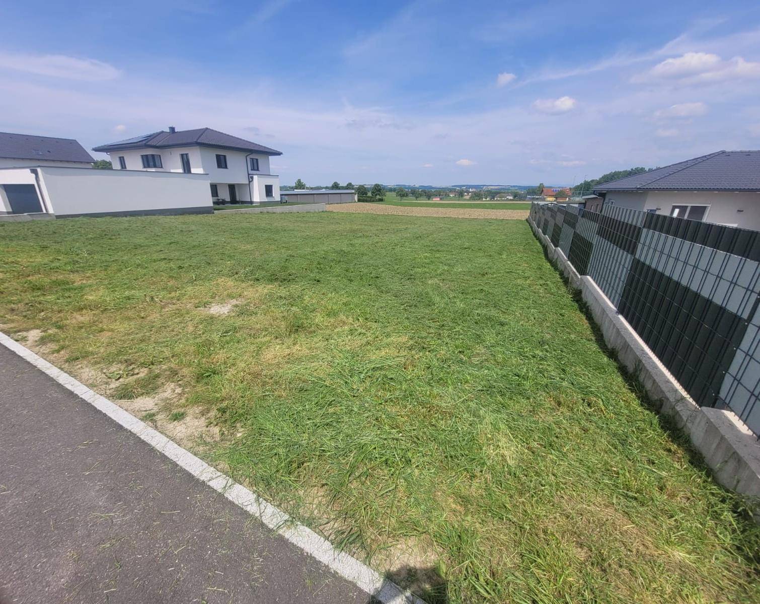 Weitläufiges Grundstück mit Grasfläche und angrenzendem Neubau in sonniger Lage.
