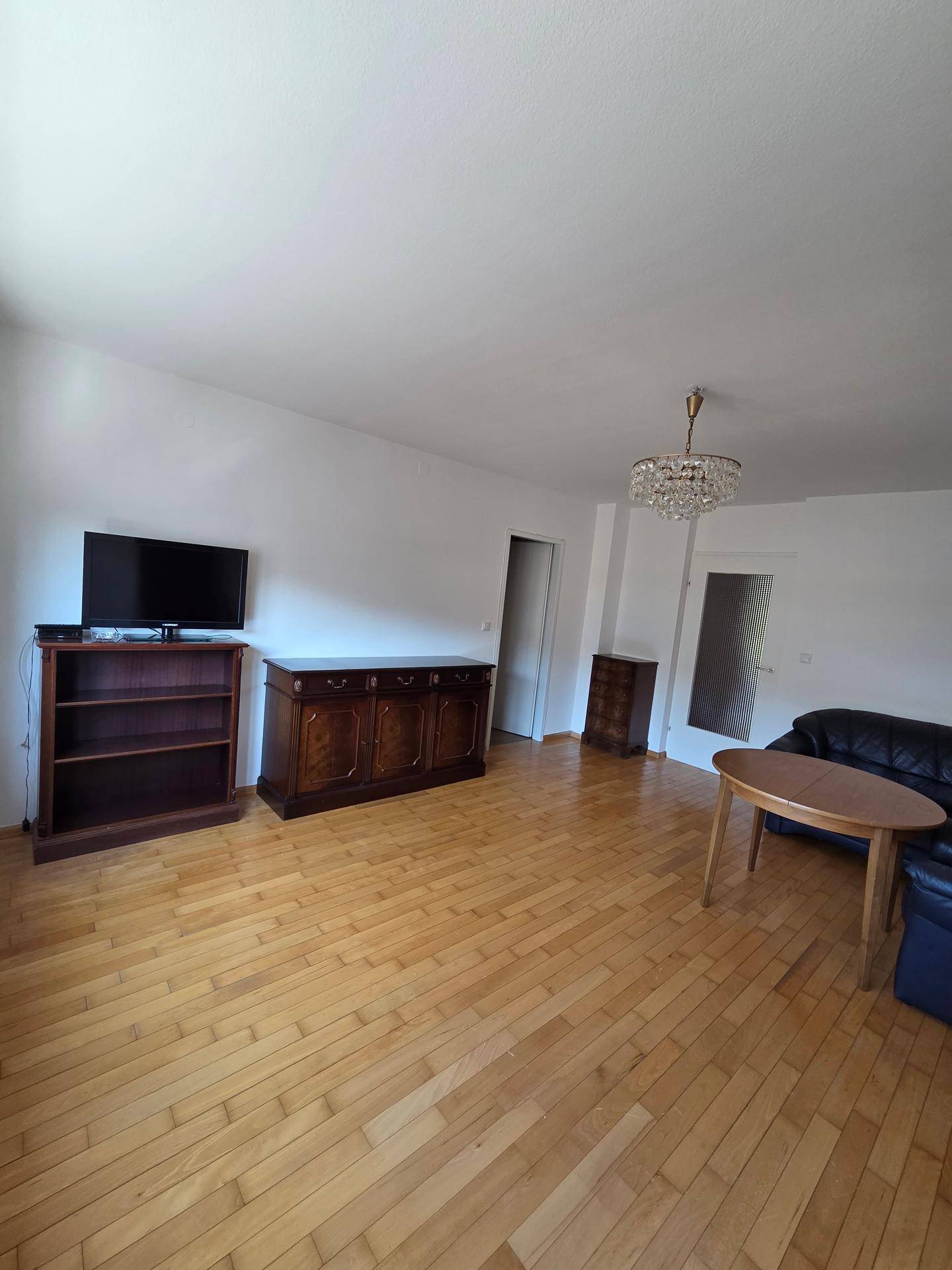 Geräumiges Wohnzimmer mit Holzboden, TV-Möbeln und Kronleuchter.