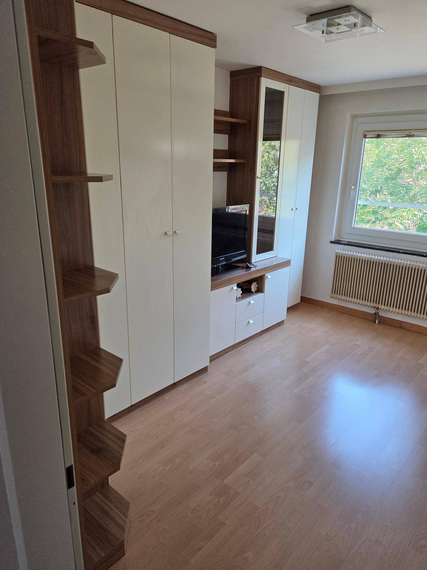 Zimmer mit Holzboden, Einbauschränken und Fenster mit Blick ins Grüne.