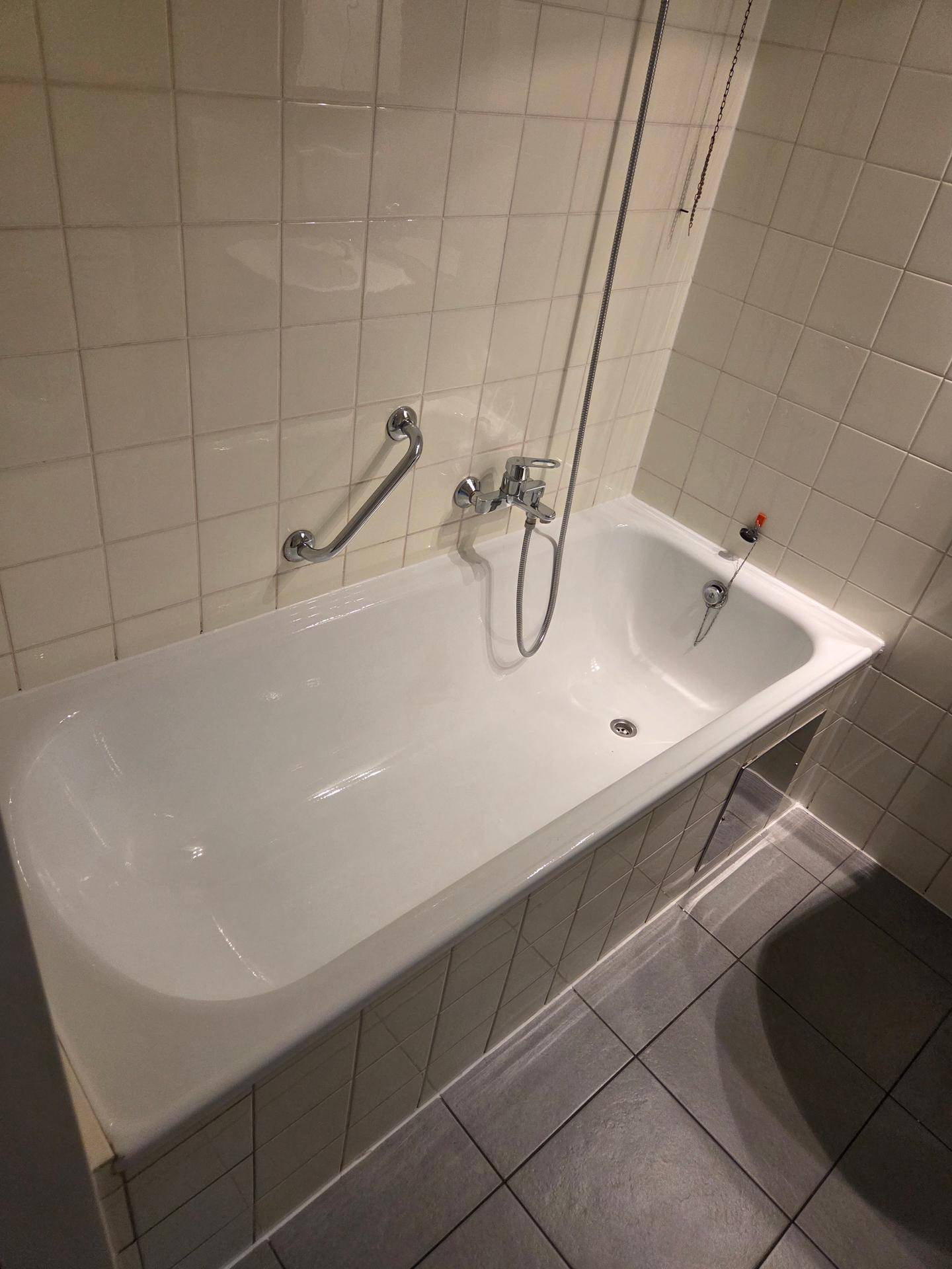 Badezimmer mit Badewanne, weißen Fliesen und Haltegriffen für mehr Sicherheit.