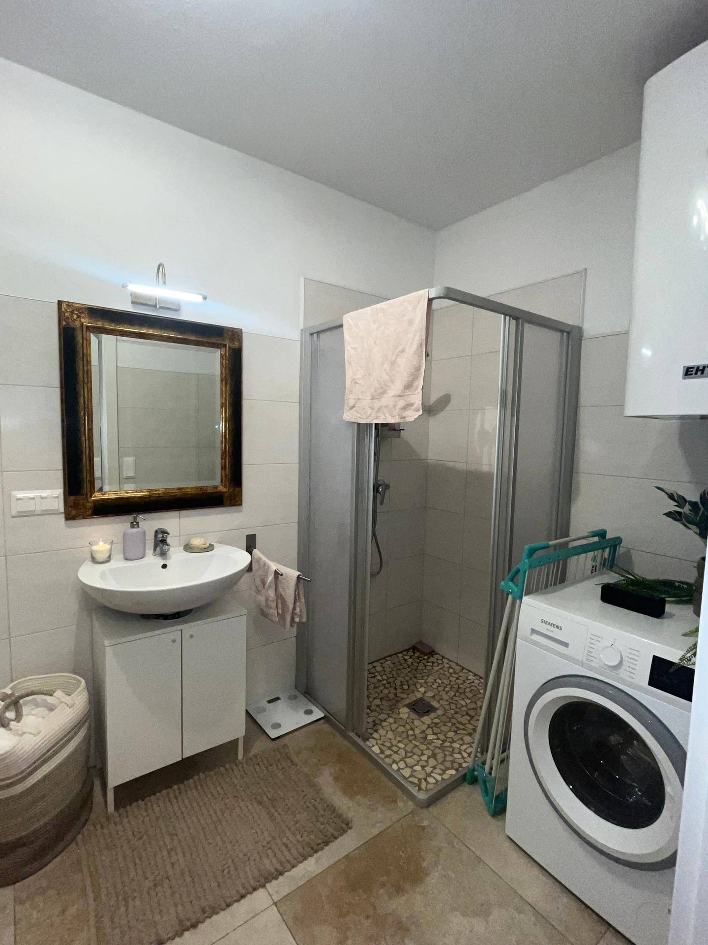 Badezimmer mit Duschkabine, Waschbecken und integrierter Waschmaschine für praktische Nutzung.