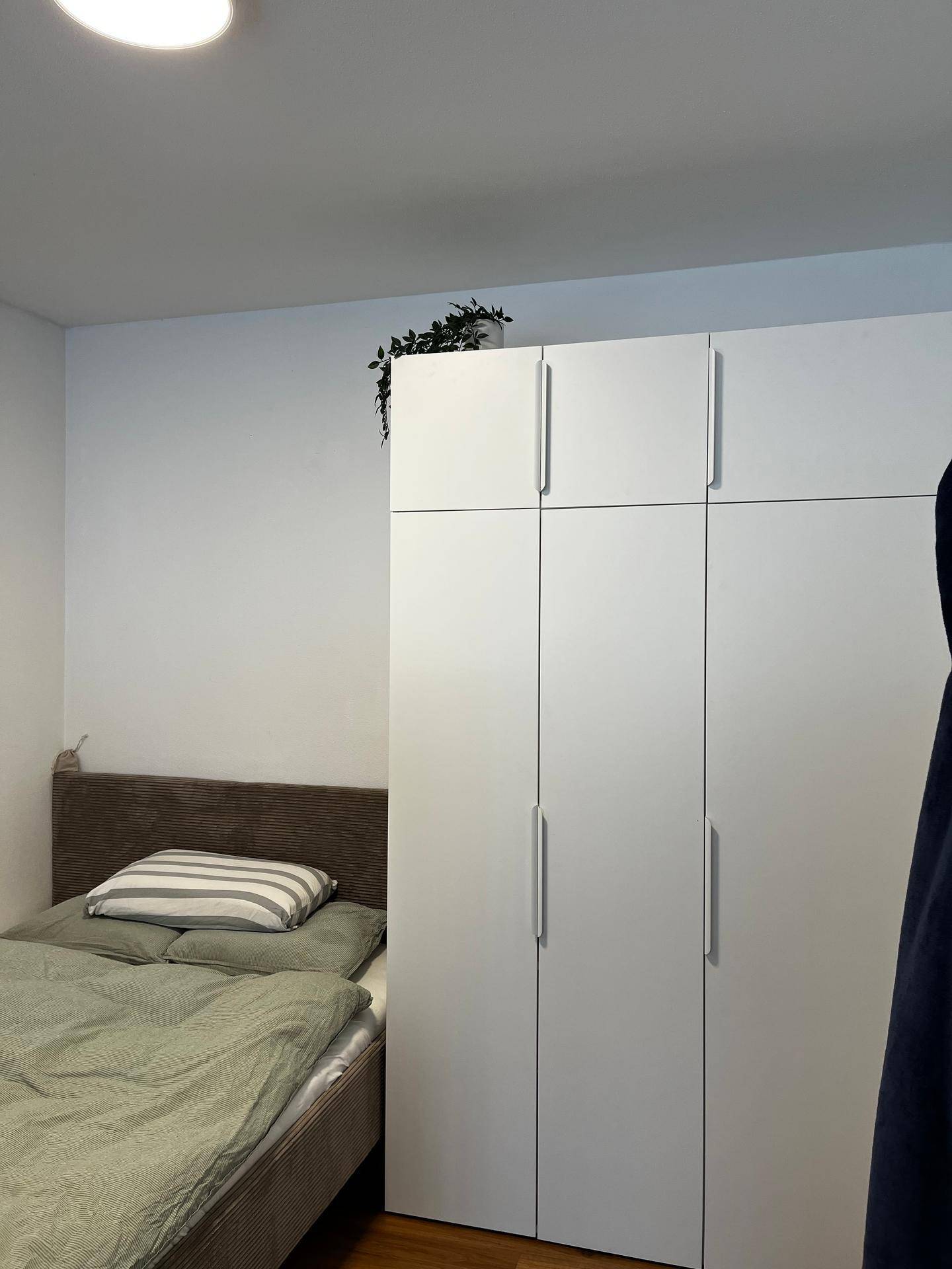 Schlafzimmer mit Einzelbett, weißem Kleiderschrank und einfacher Dekoration für eine ruhige Nacht.