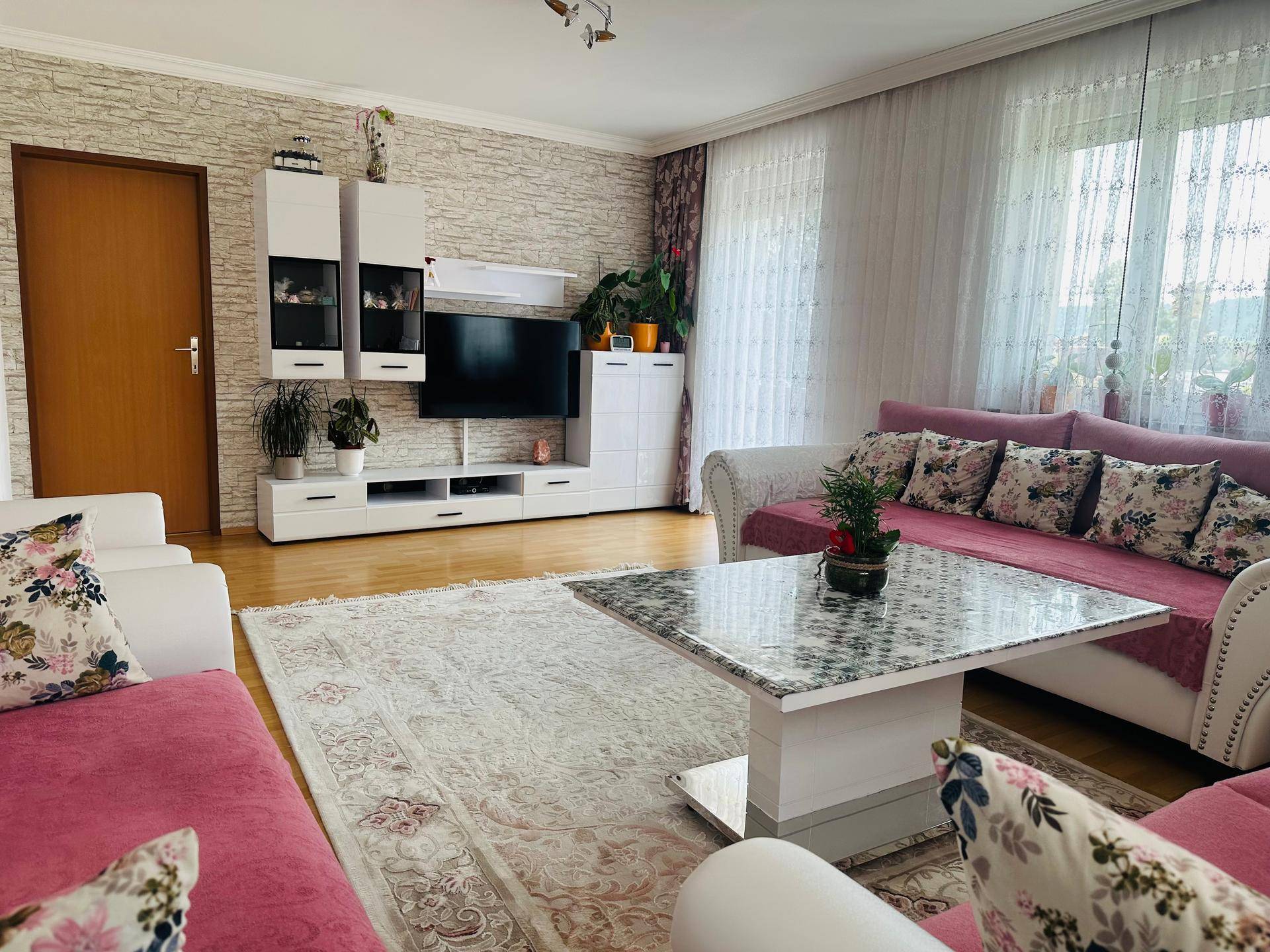 Helles Wohnzimmer mit rosa Sofas, modernem TV-Möbel und gemustertem Teppich.