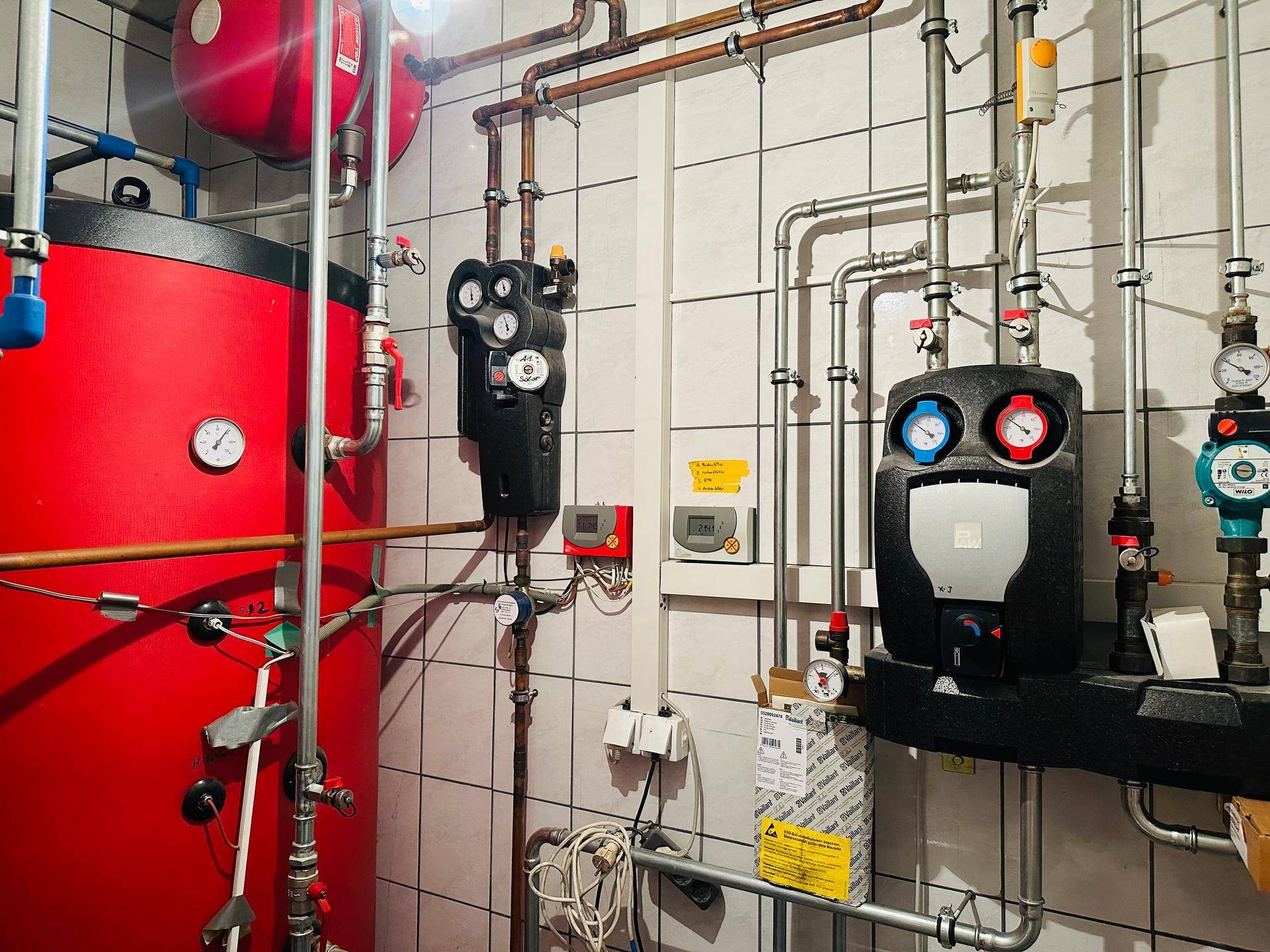 Technikraum mit großen roten Wassertanks, zahlreichen Rohren und gefliesten Wänden.