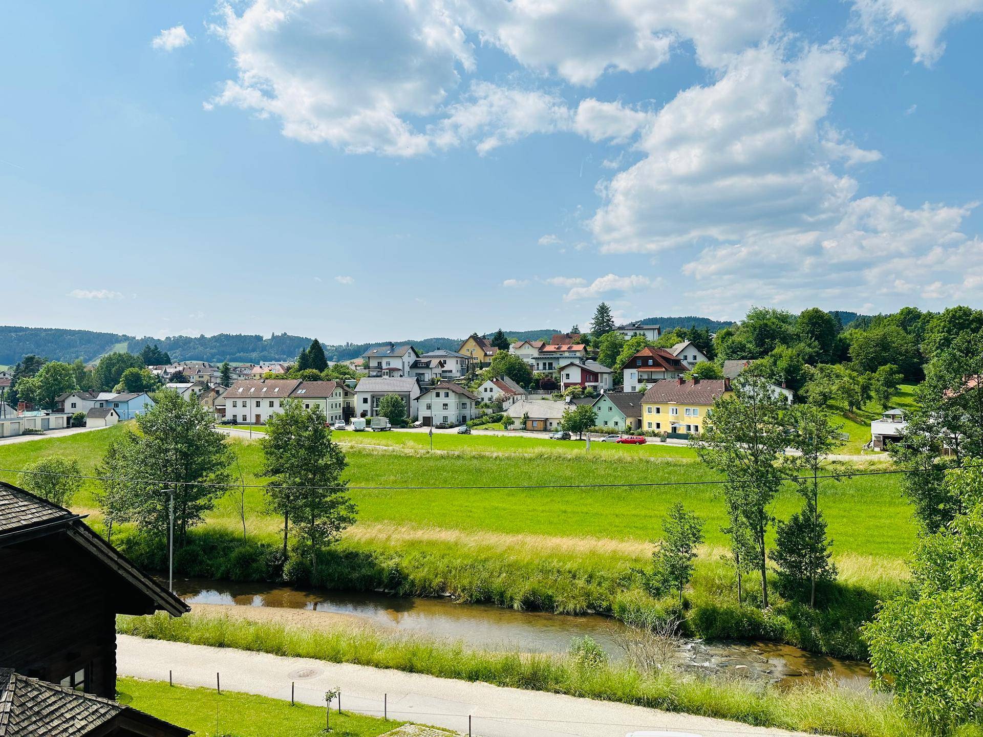 Malerischer Blick auf ein Dorf in einem grünen Tal mit Fluss und weitem Himmel.