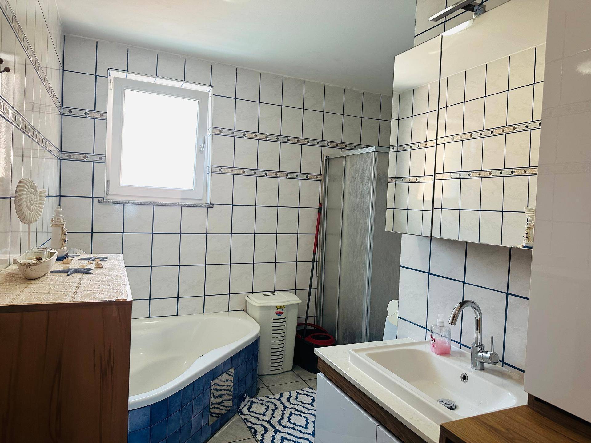 Gefliestes Badezimmer mit Badewanne, Duschkabine, Einzelwaschbecken und Fenster.