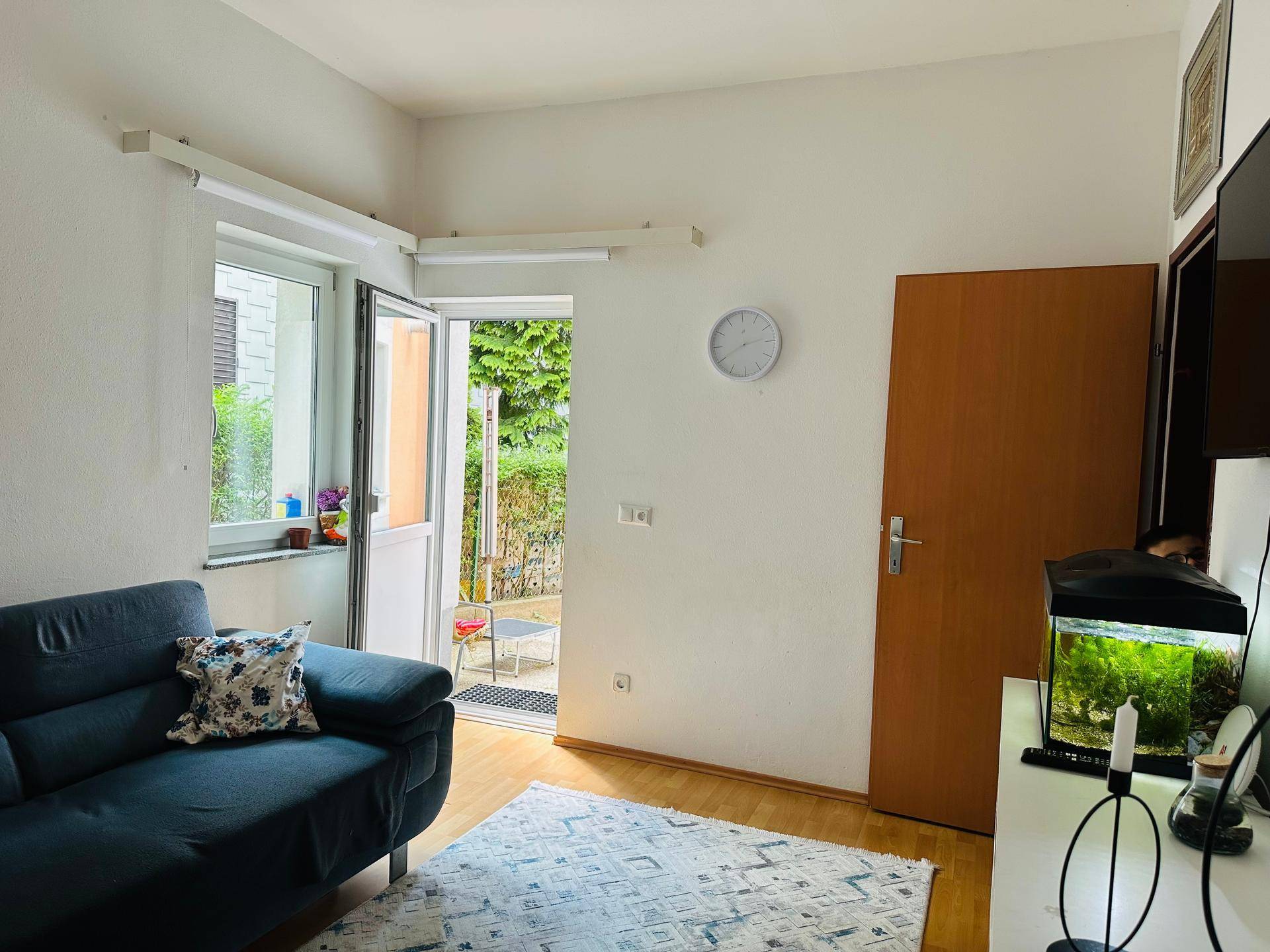 Gemütliches Wohnzimmer mit blauem Sofa, Holzboden und direktem Zugang zum Gartenbereich.