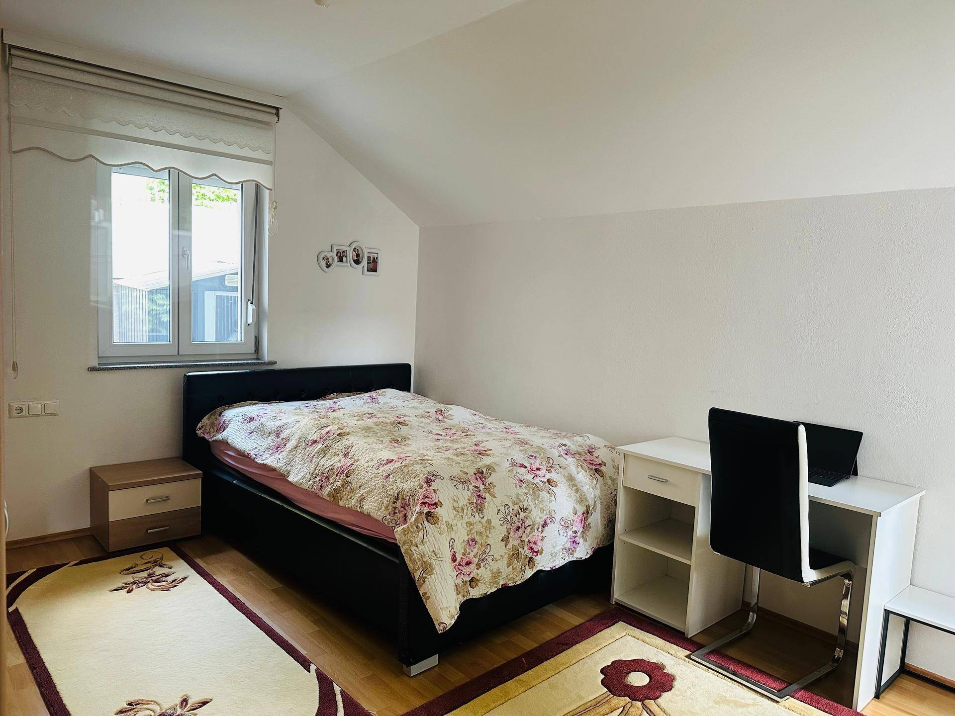 Schlafzimmer mit Einzelbett, Schreibtisch und Fenster, unter einer Dachschräge gelegen.