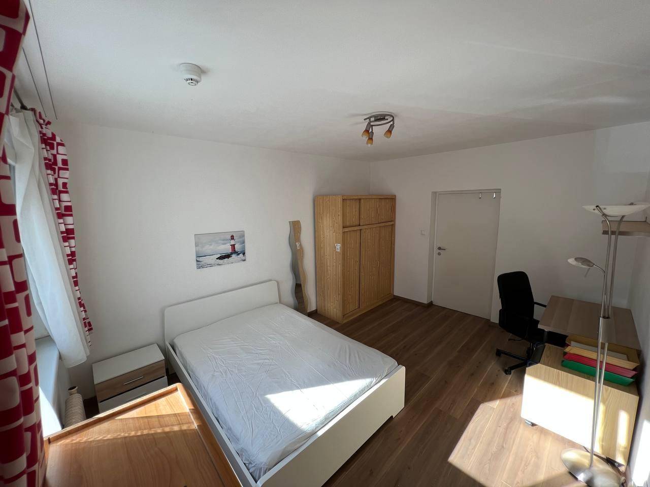Gemütliches Schlafzimmer mit Holzboden, Einzelbett, Nachttisch und Schreibtisch.