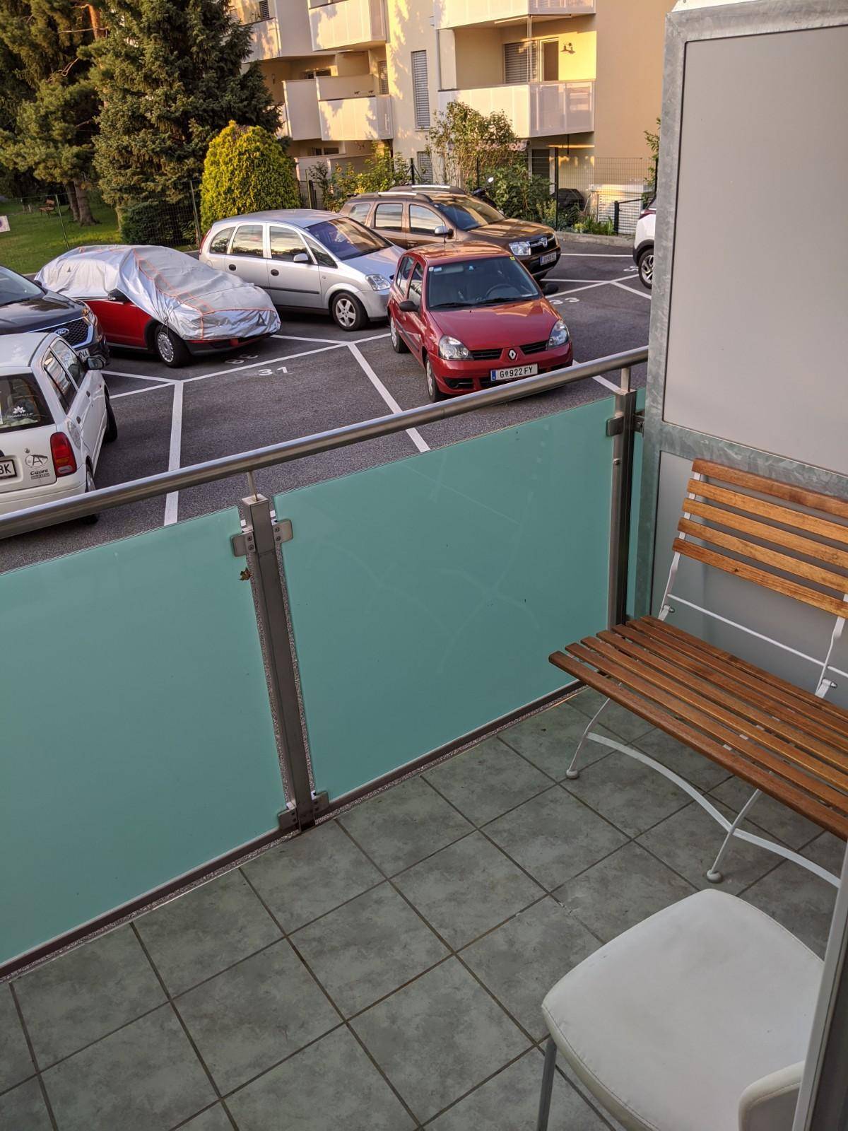Balkon mit Fliesenboden und Sitzgelegenheit, Blick auf den Parkplatz.