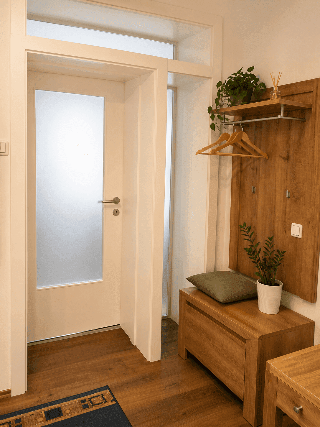 Heller Flur mit Garderobe aus hellem Holz und einer Tür mit Milchglas-Einsatz.