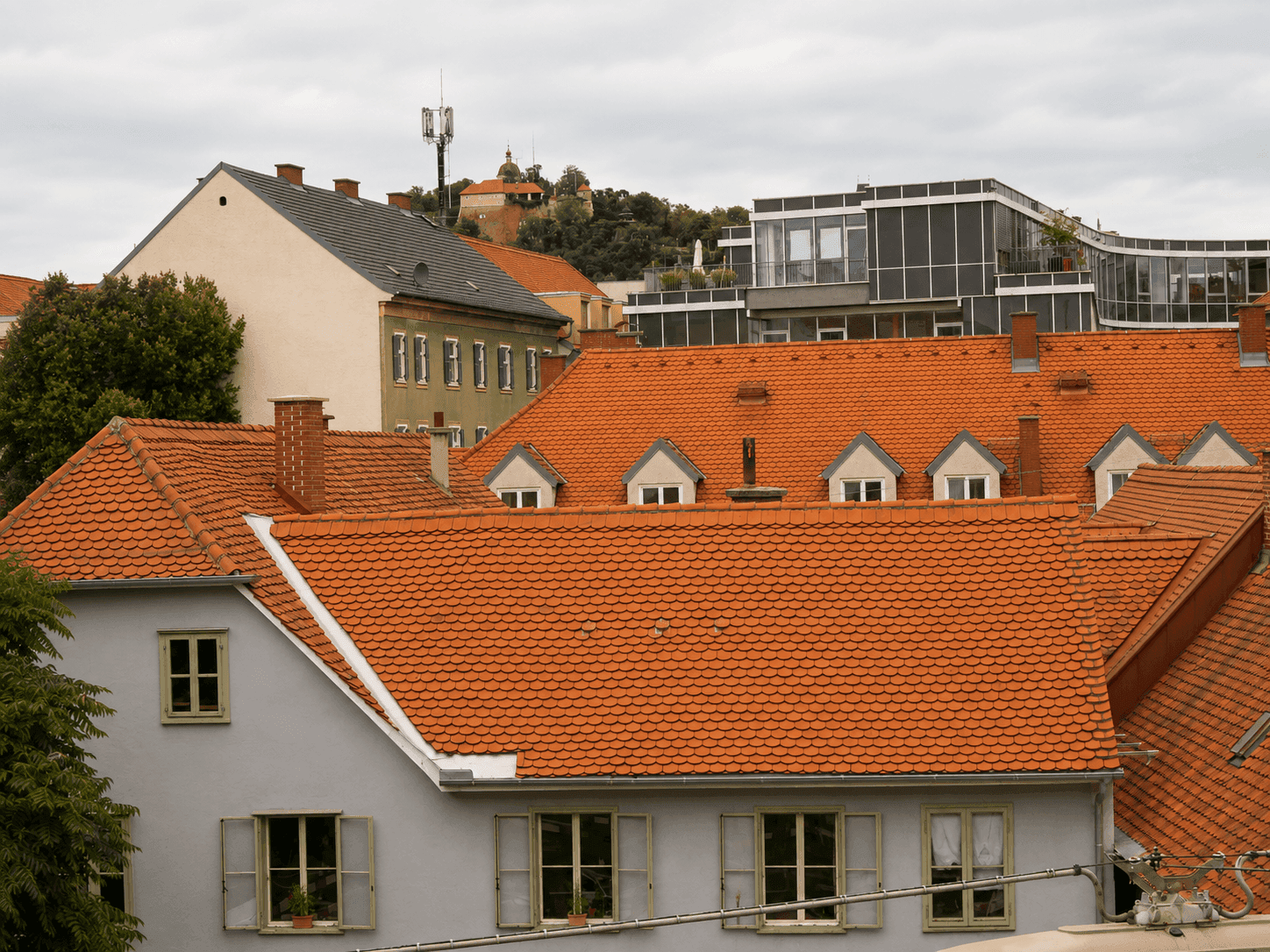 Blick über die Dächer der Stadt mit traditionellen Ziegeldächern und modernen Gebäuden im Hintergrund.