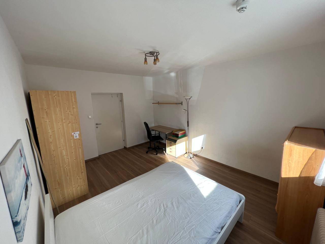 Weitläufiges Schlafzimmer mit Holzboden, Bett, Schreibtisch und Kleiderschrank.