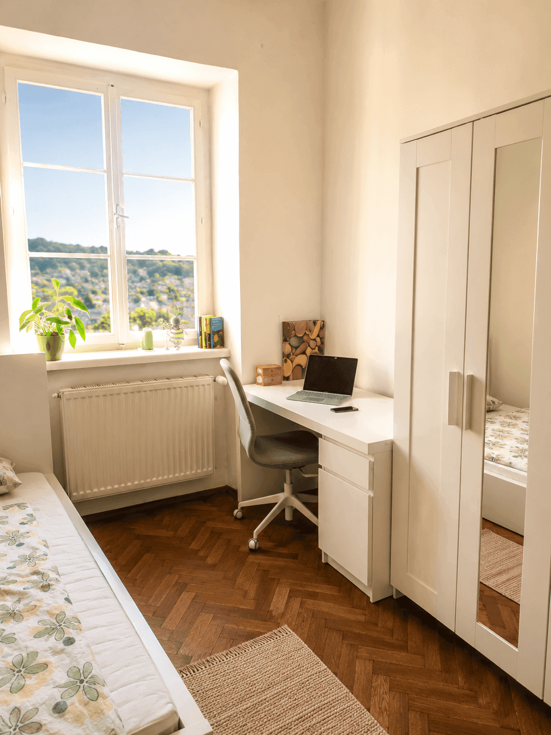 Detailansicht des hellen Schlafzimmers mit Schreibtisch am Fenster und Blick ins Grüne.