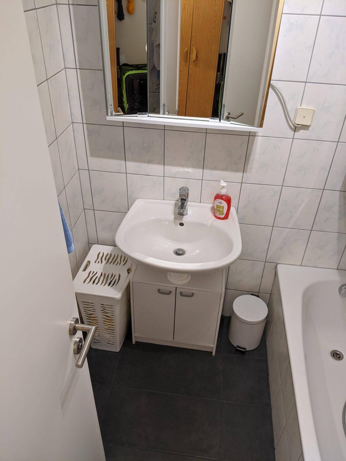 Badezimmer mit Waschbecken, Spiegelschrank und weißen Fliesen.