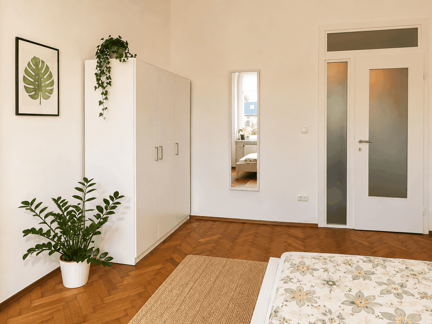 Schlafzimmer mit Parkettboden, weißem Kleiderschrank und Tür mit Milchglas-Einsatz.
