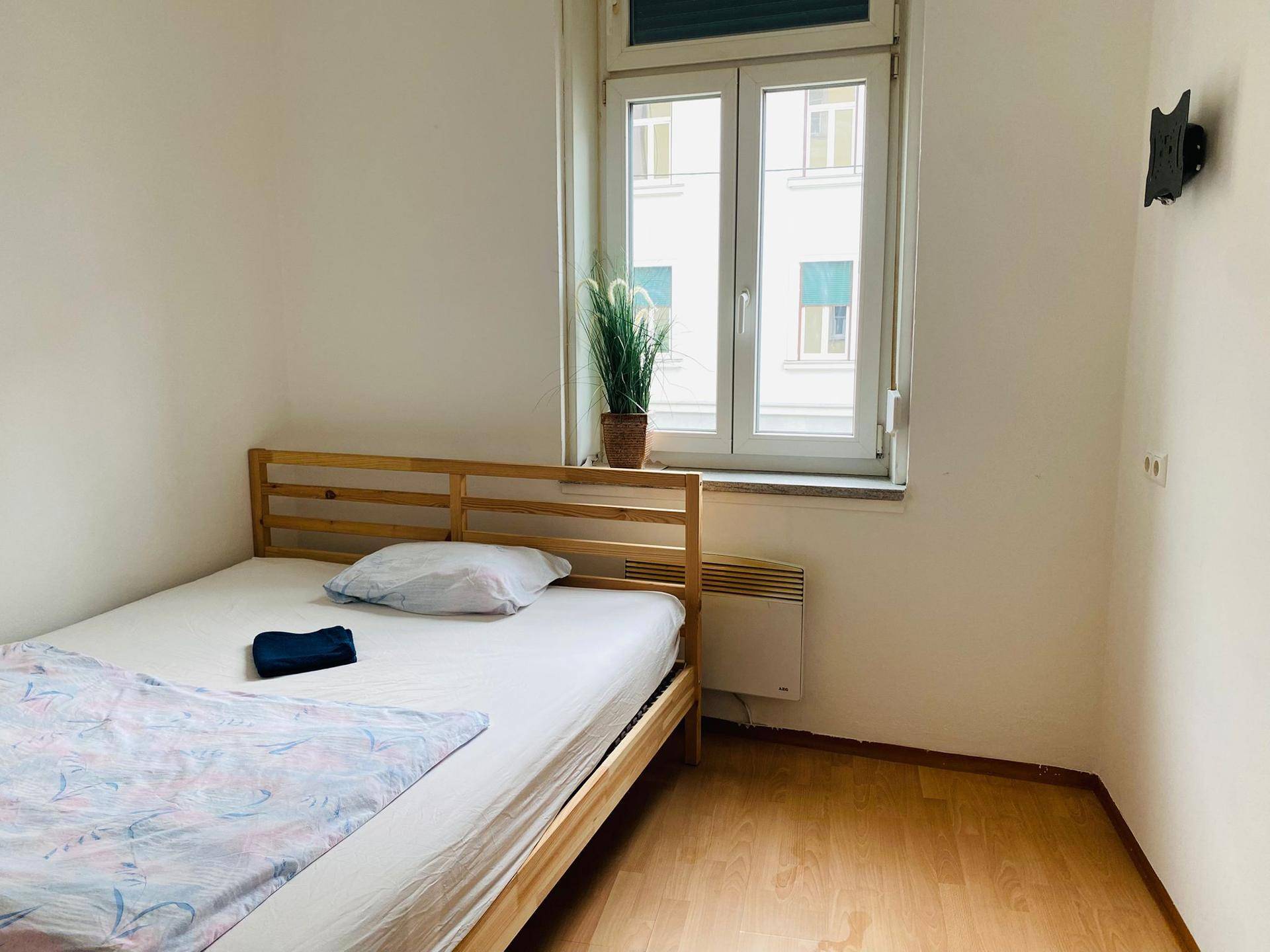 Helles Schlafzimmer mit Einzelbett, Holzrahmen und Blick aus dem Fenster auf die Stadt.