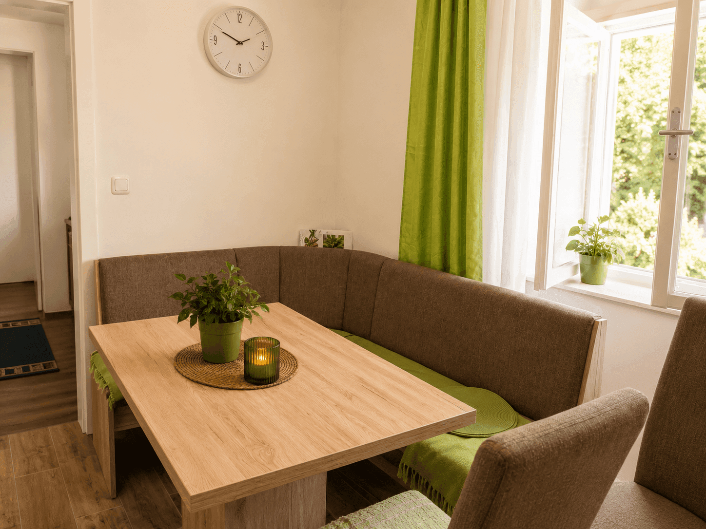 Heller Essbereich mit Eckbank, Holztisch und grünen Akzenten am Fenster mit Blick ins Grüne.