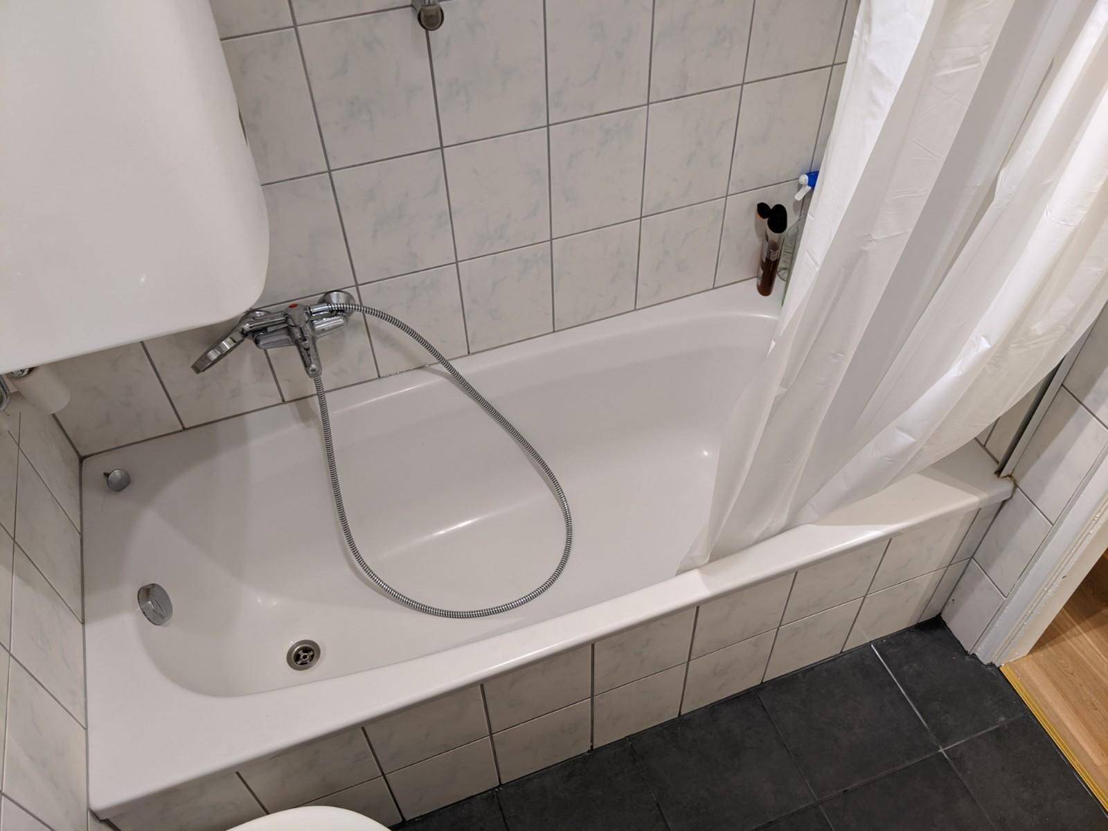 Badezimmer mit Badewanne und weißen Wandfliesen, funktional eingerichtet.