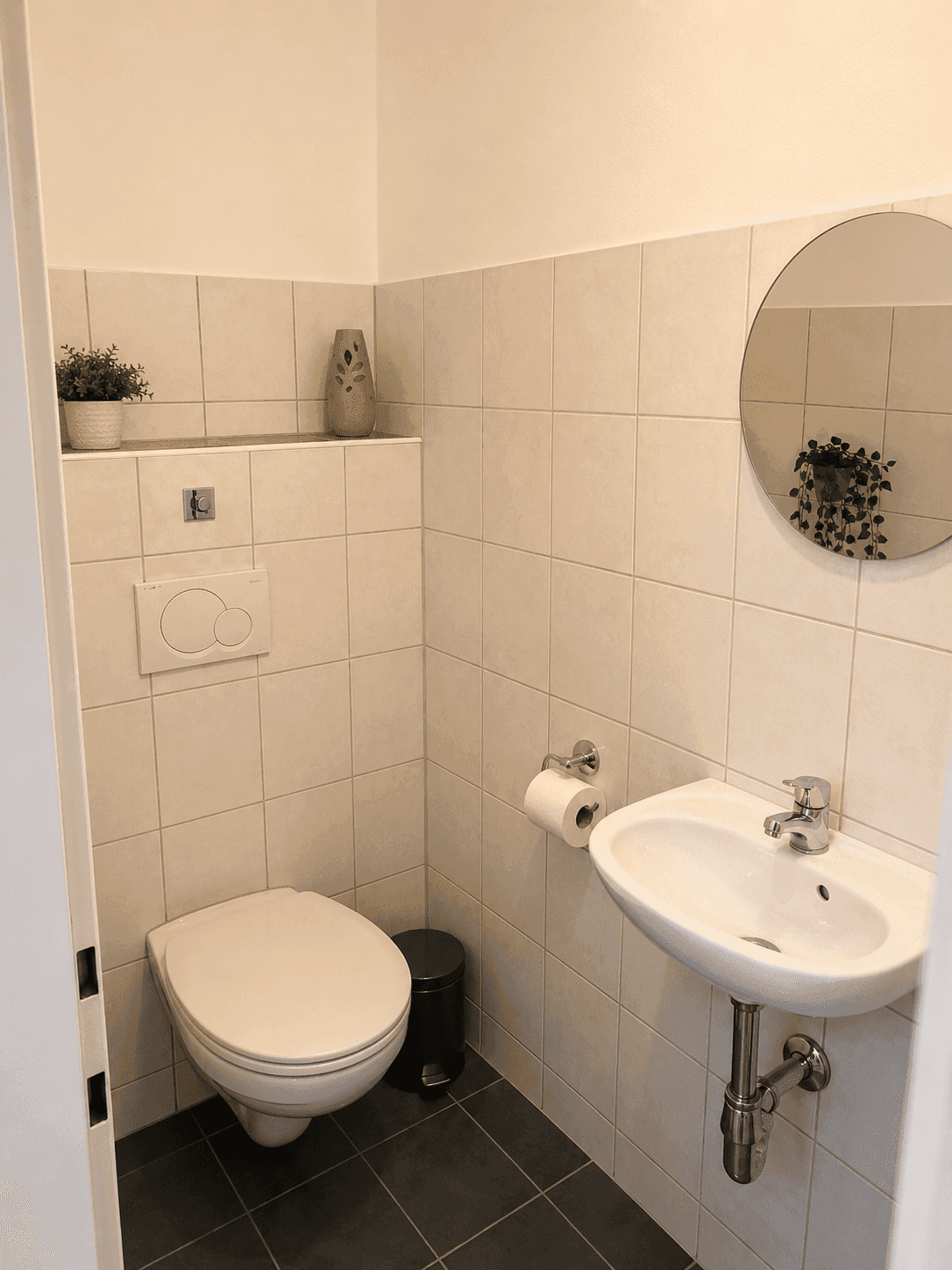 Kleines Gäste-WC mit Wand-WC, Waschbecken und hellen Fliesen an den Wänden.