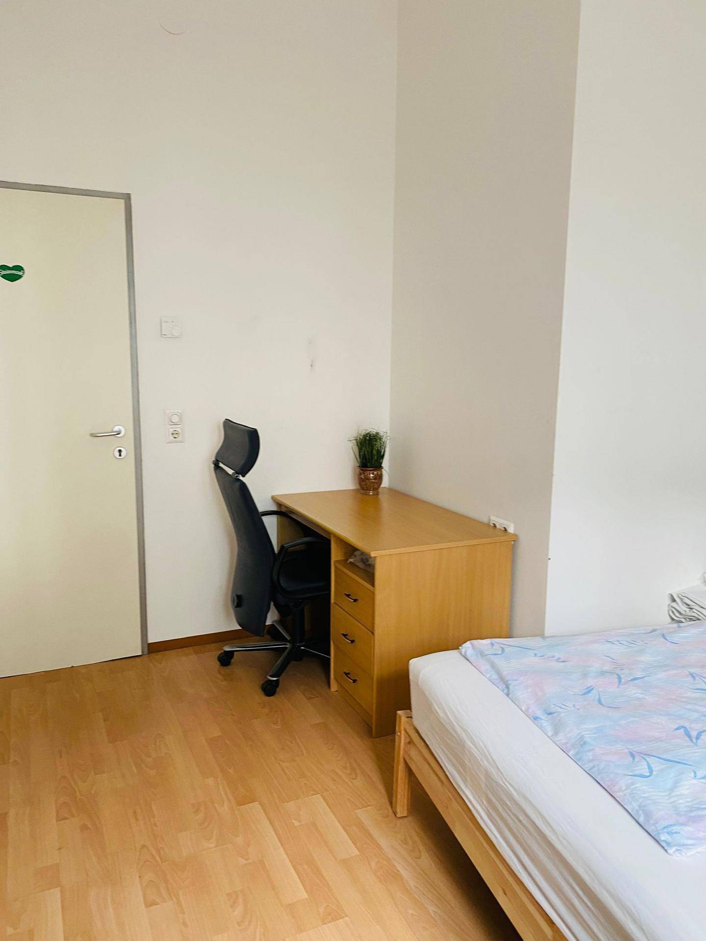 Funktional eingerichtetes Schlafzimmer mit Schreibtisch, Bürostuhl und hellem Holzfußboden.