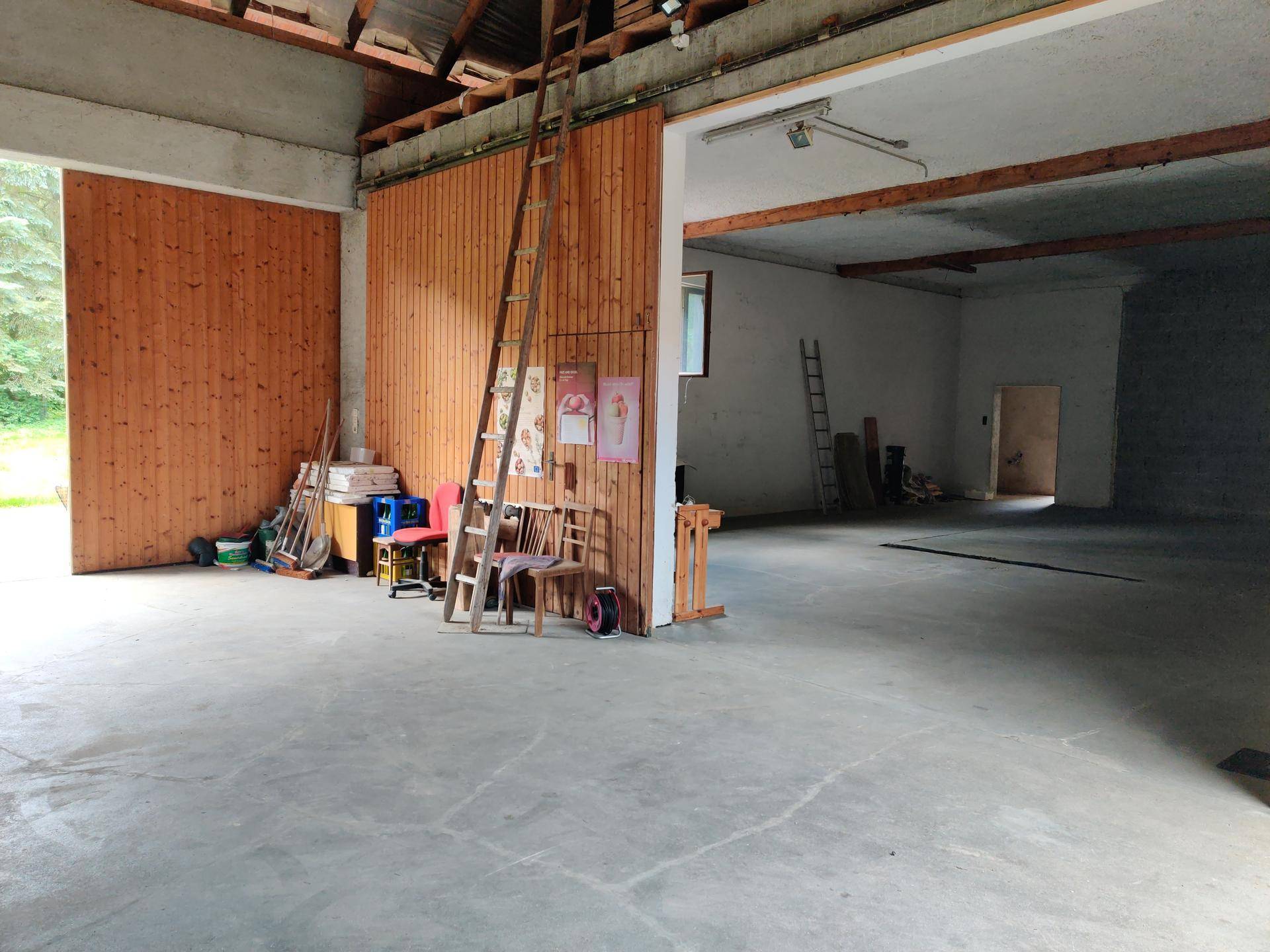 Geräumiger Werkstattbereich mit Betonboden, Holzverkleidung und einem großen Tor zum Außenbereich.