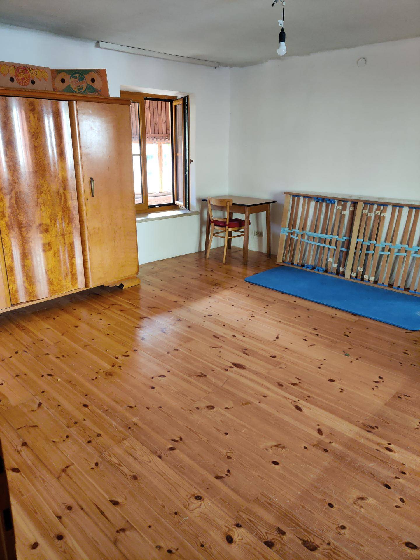 Helles Schlafzimmer mit Holzdielenboden, einem Kleiderschrank und einem Fenster mit Blick nach draußen.